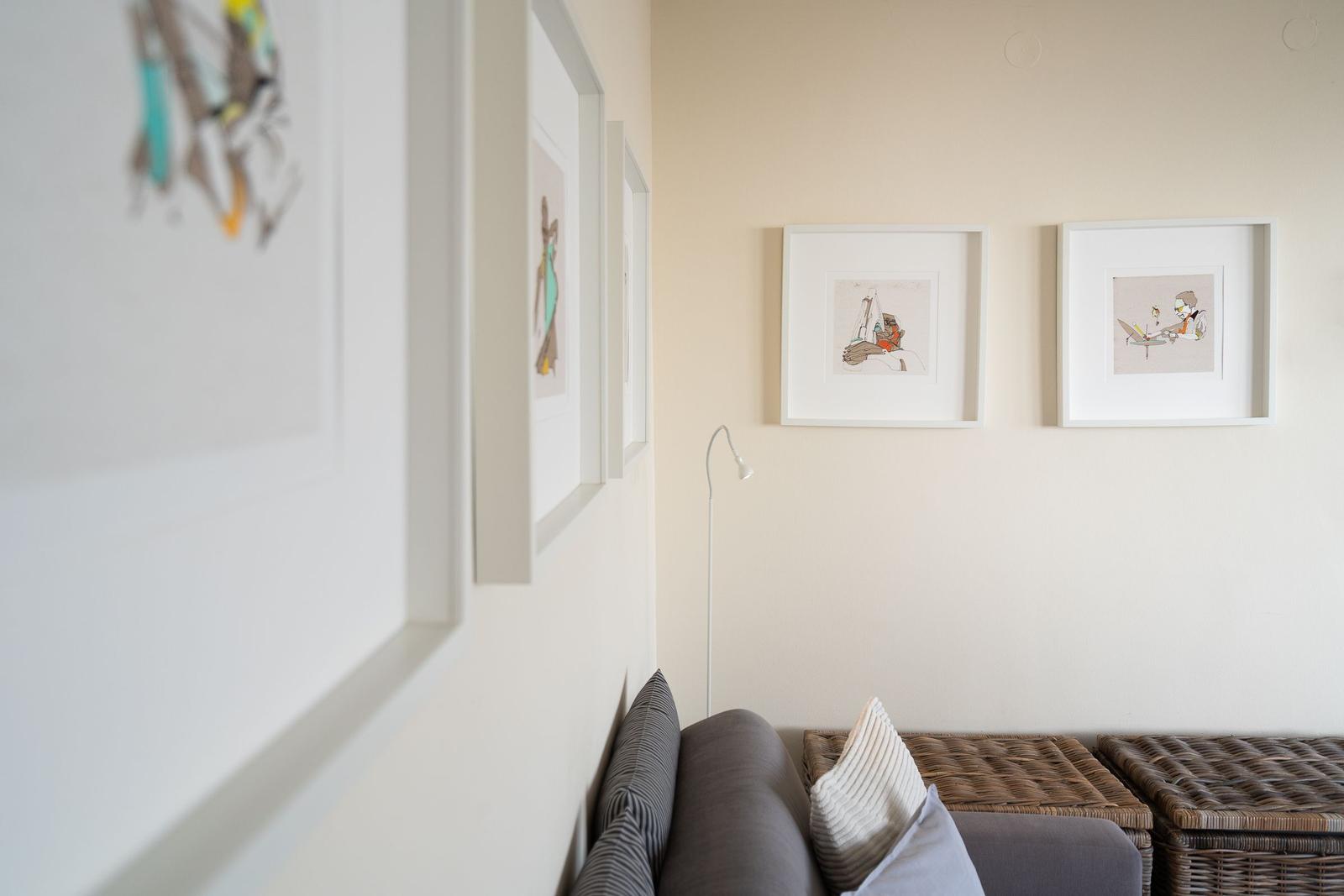 Wohnbereich mit Sofa, Korbhocker und Wandbildern.