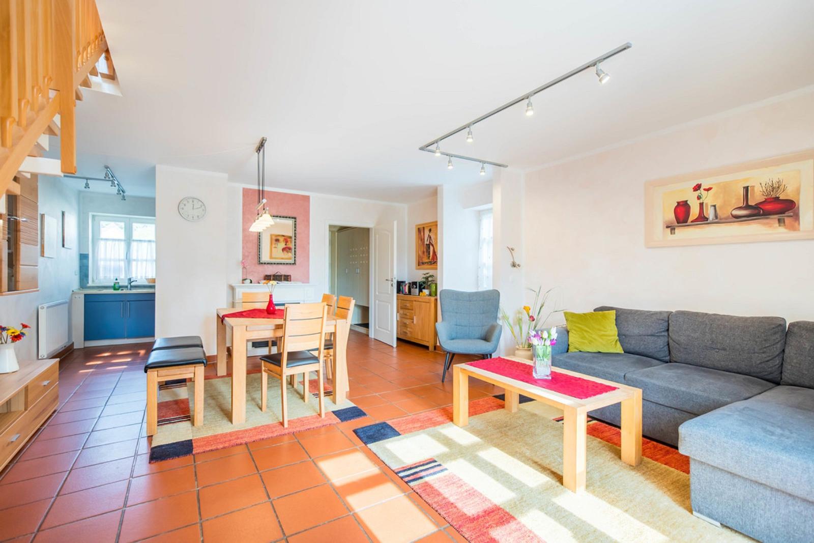 Wohn- und Essbereich mit Sofa, Tisch und Stühlen. Terrakottaboden und Holzmöbel.