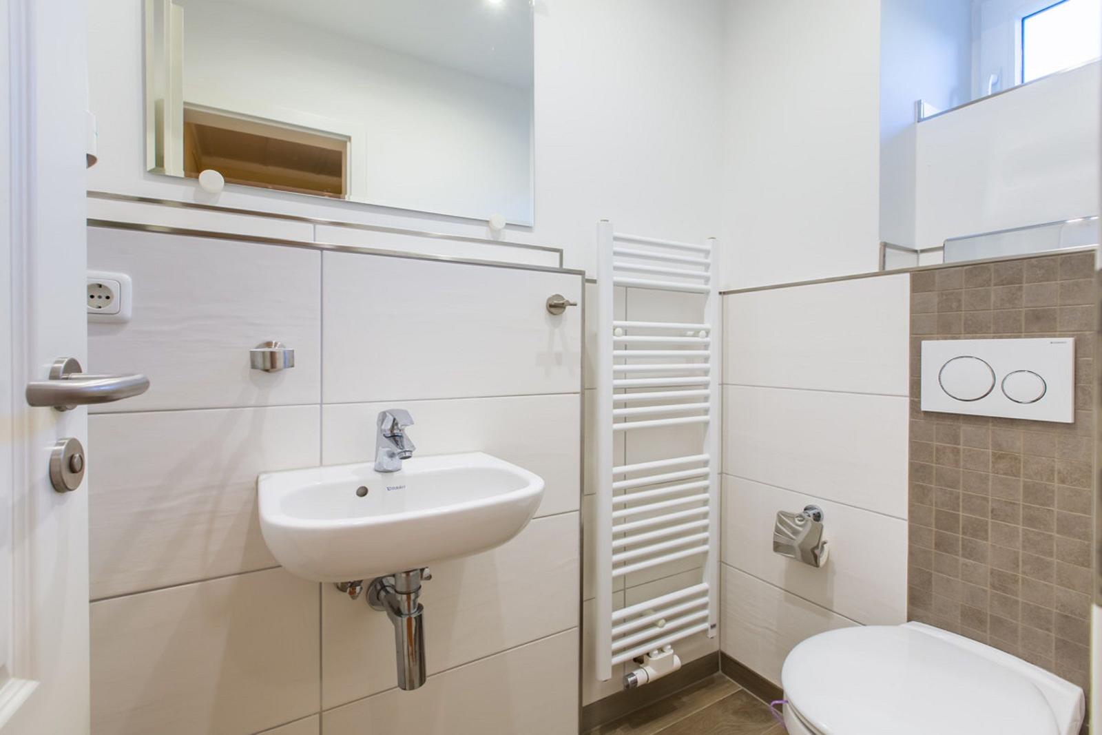 Badezimmer mit Waschbecken, Spiegel, Heizkörper und Toilette.