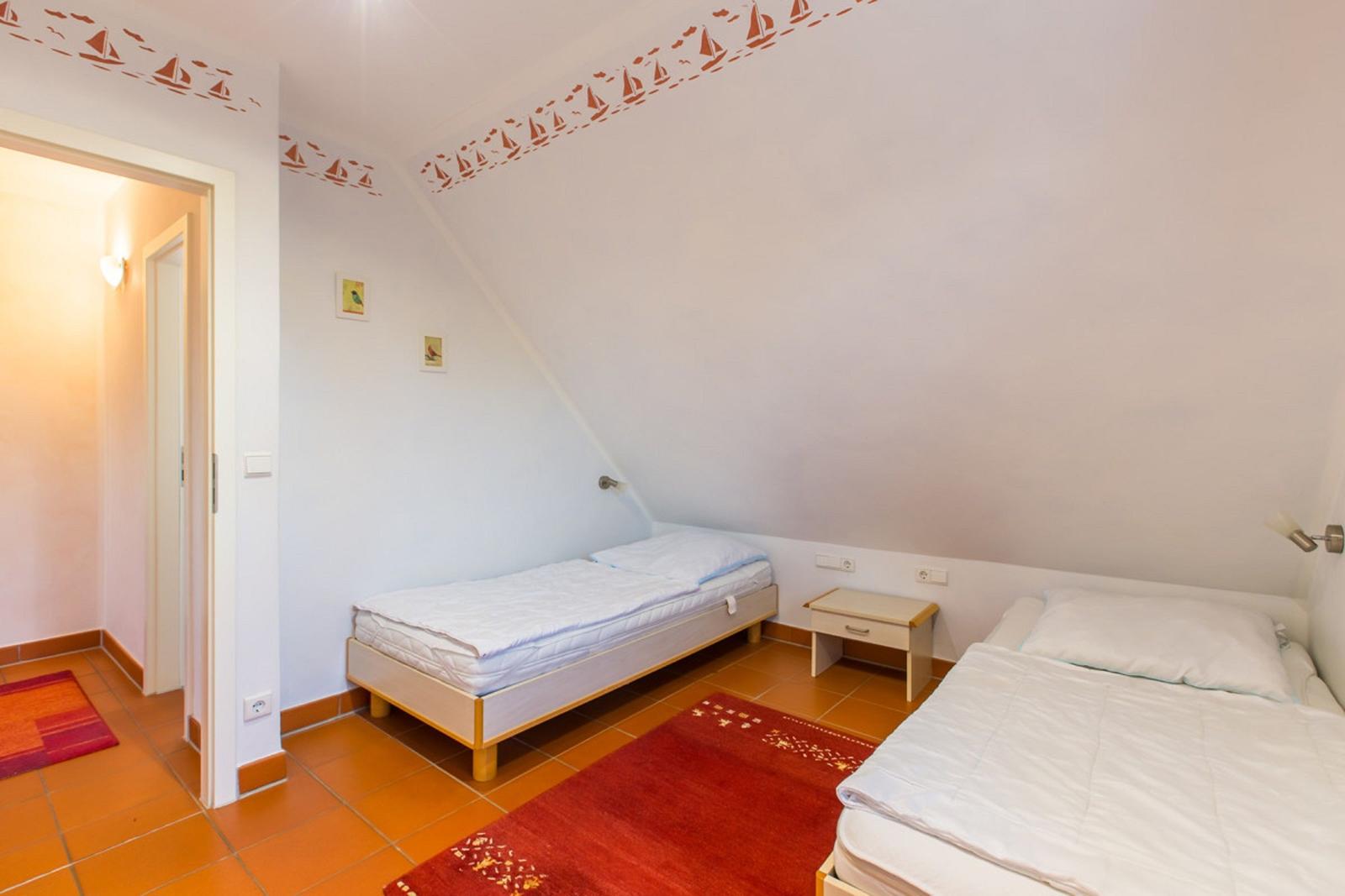Zimmer mit zwei Betten, rotem Teppich und Wanddekoration mit Segelbooten.