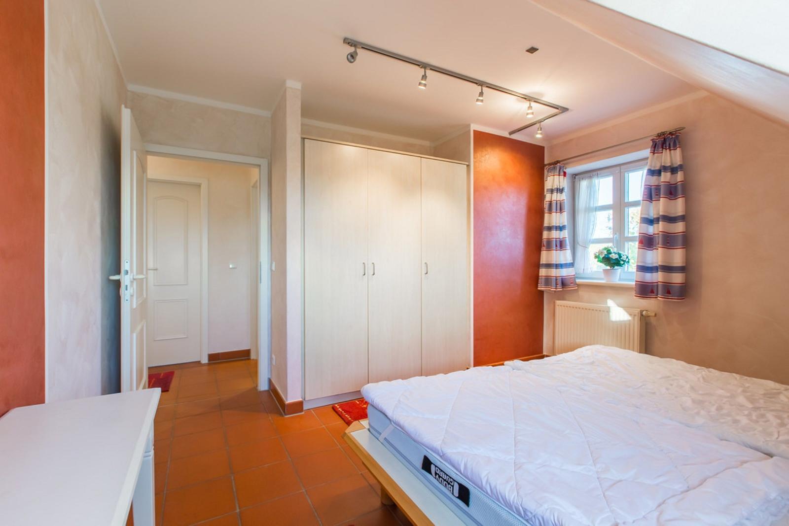 Schlafzimmer mit Bett, Kleiderschrank und Fenster mit Vorhängen.