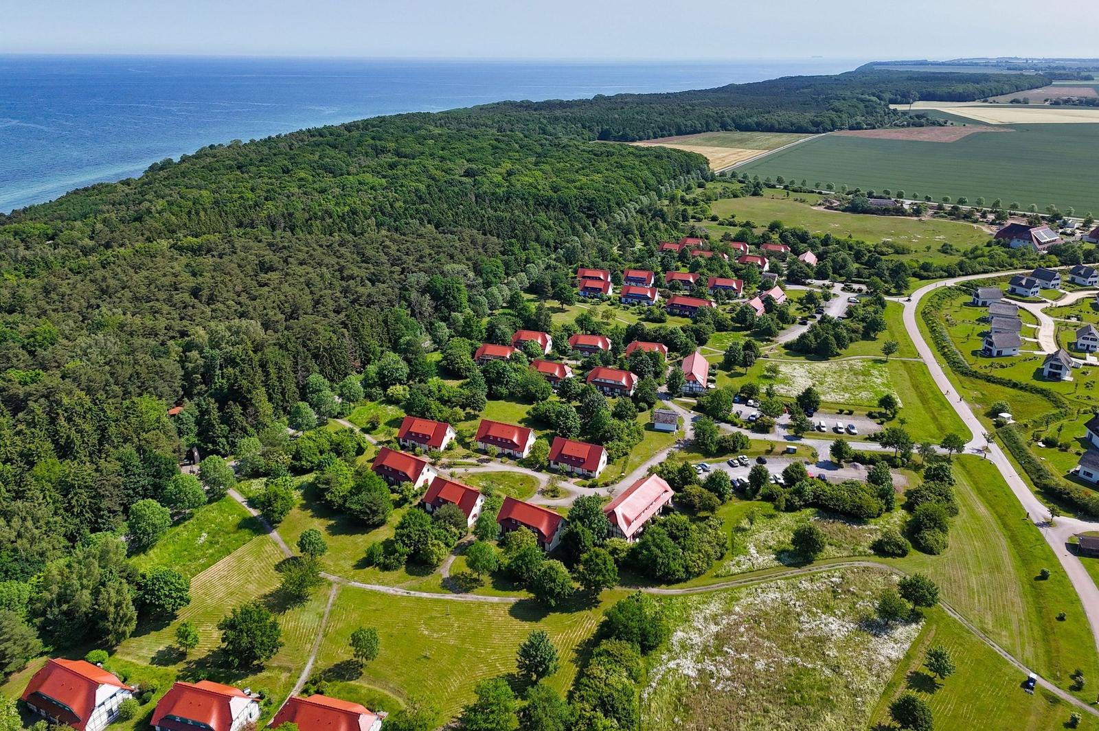 Liegenschaft mit roten Dächern, umgeben von Wald und Feldern, nahe dem Meer.
