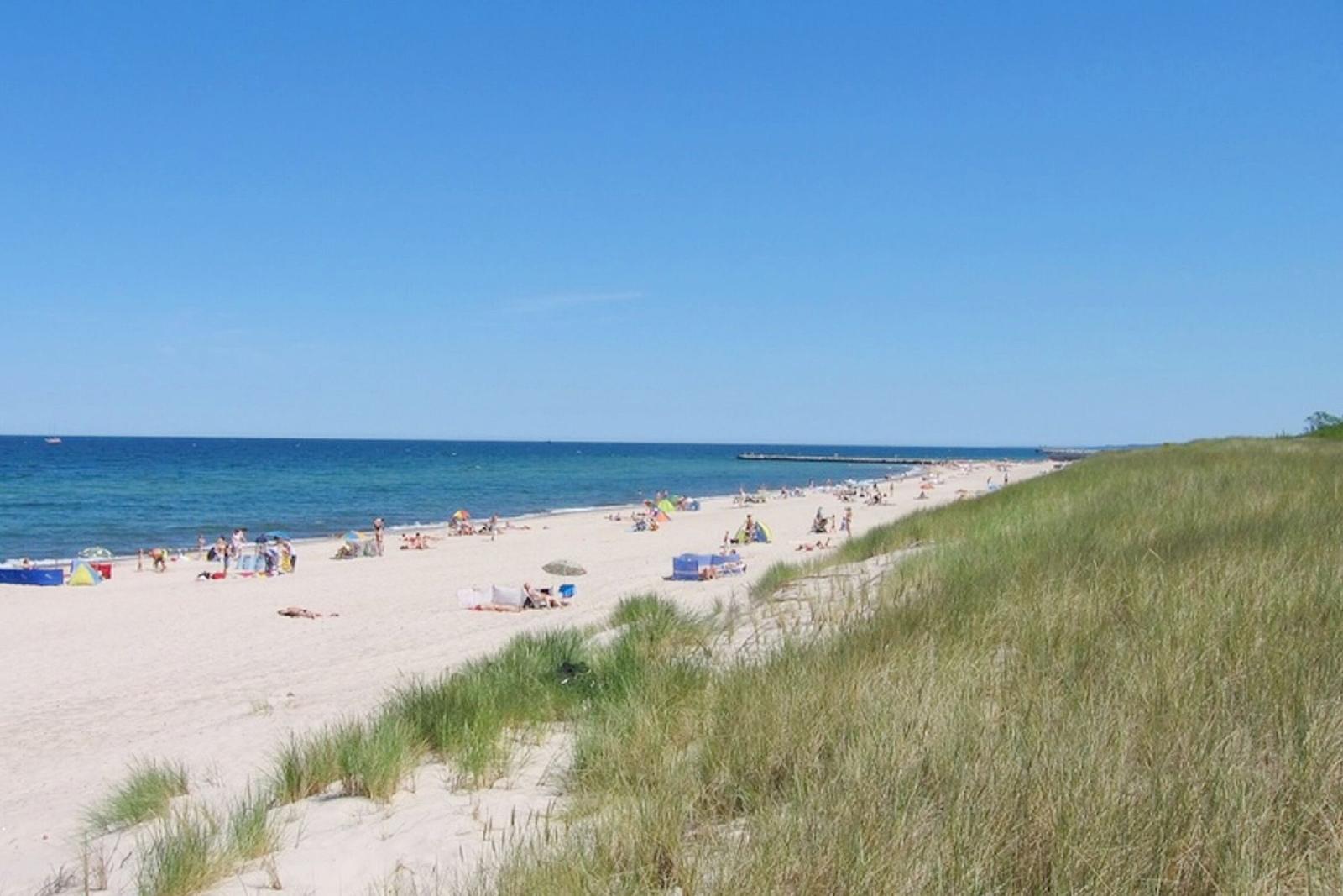 Strand mit Sanddünen und Menschen am Meer unter blauem Himmel.