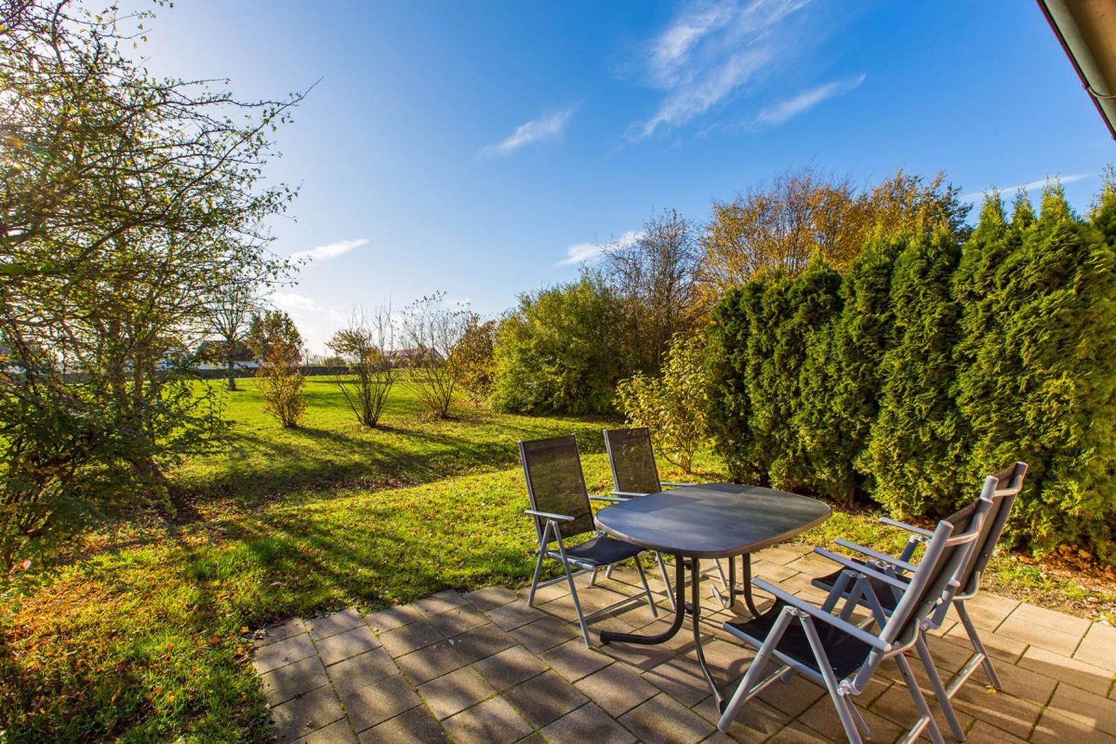 Terrasse mit Tisch und Stühlen, Blick auf grünen Garten und Hecken.