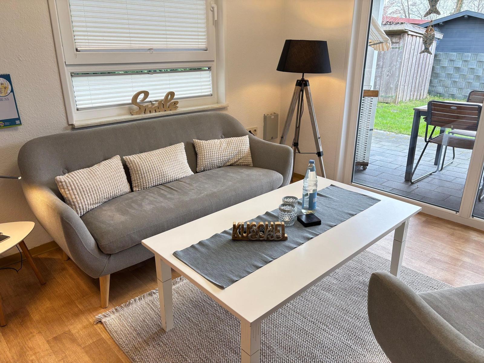 Ein Wohnzimmer mit grauem Sofa, weißem Tisch und Blick auf die Terrasse.
