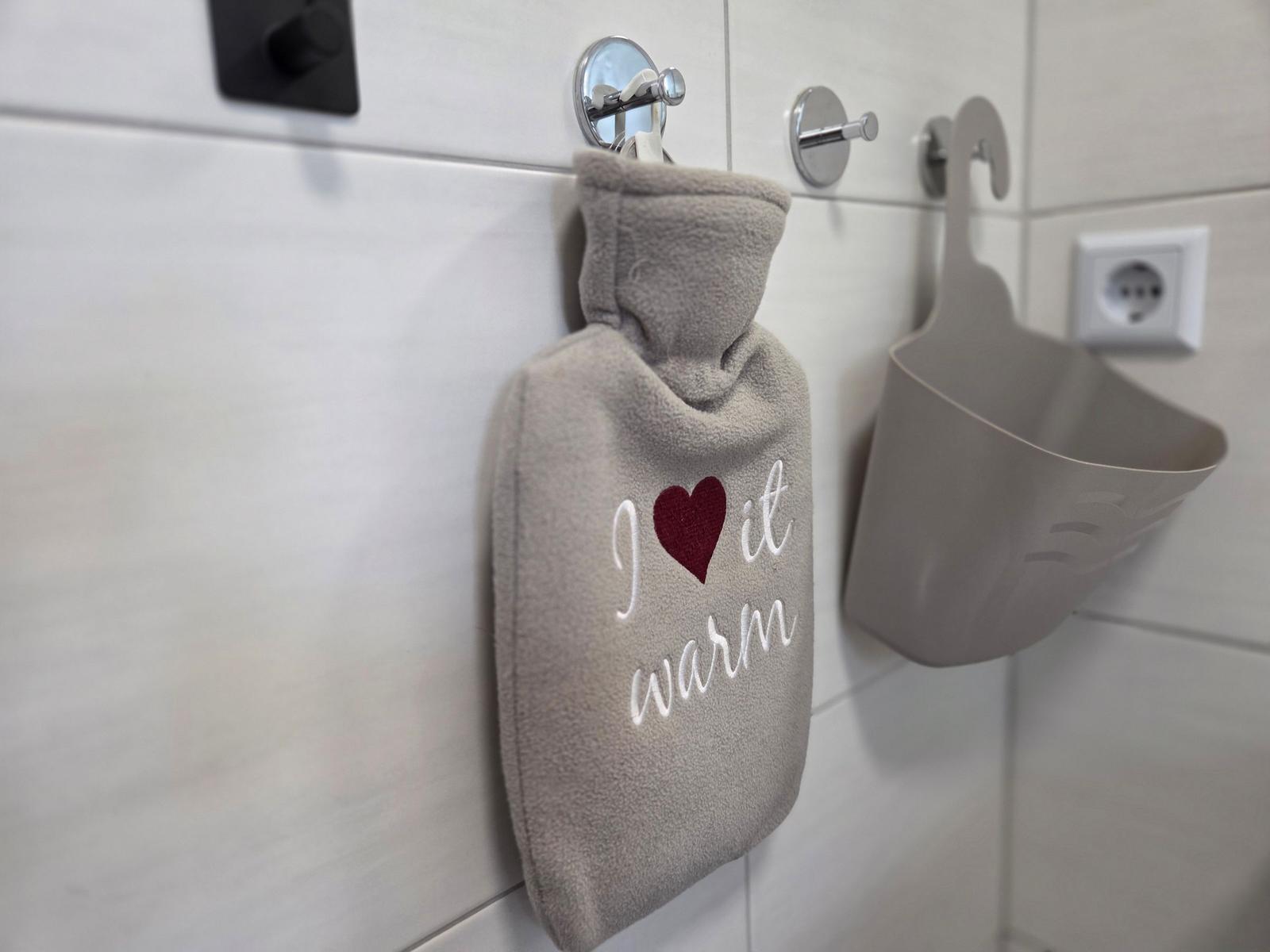 Wärmflasche mit Aufschrift hängt an Wandhalterung im Badezimmer.