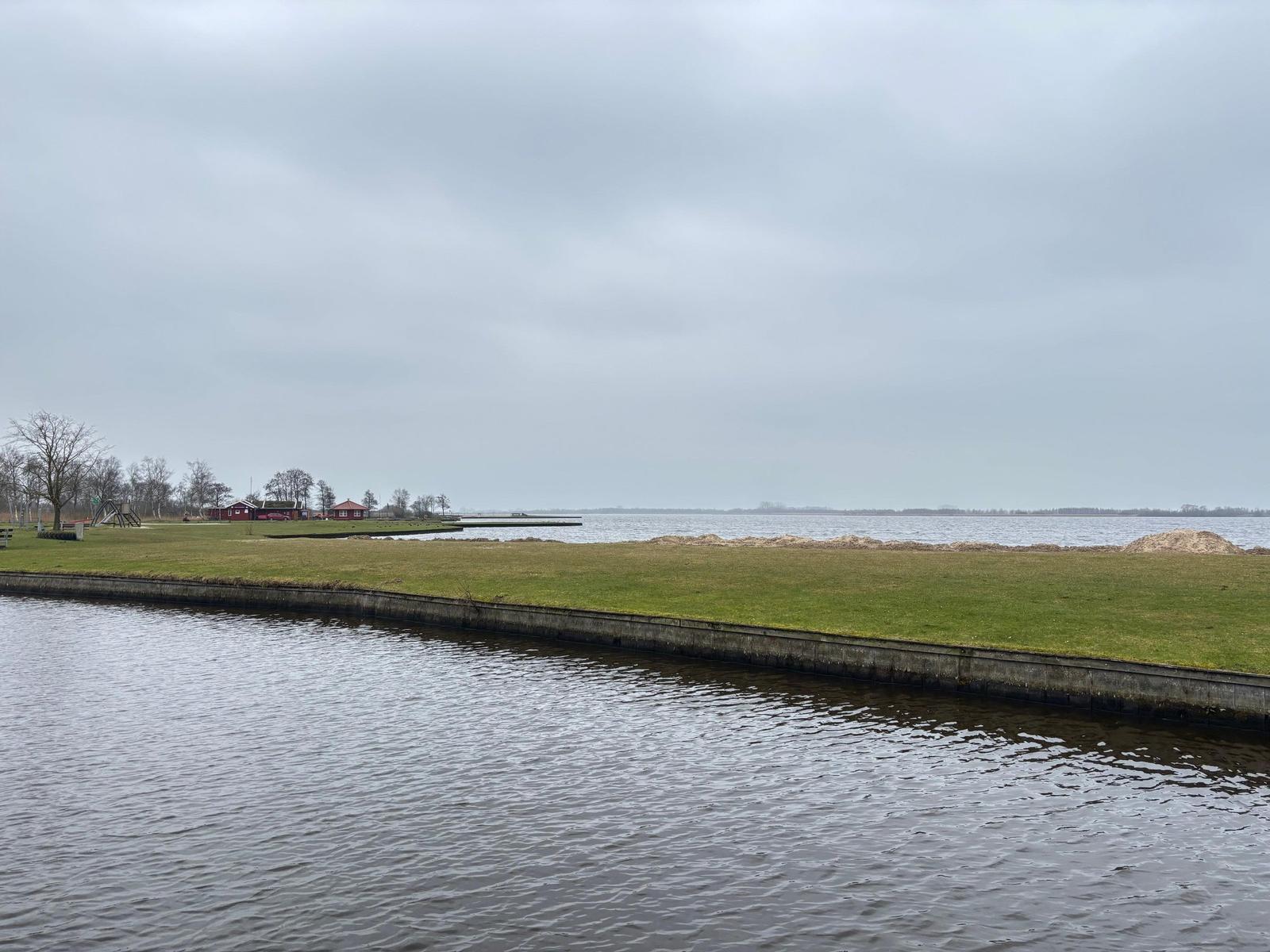 Wasserkanal mit Grasfläche und Blick auf See und rote Häuser.