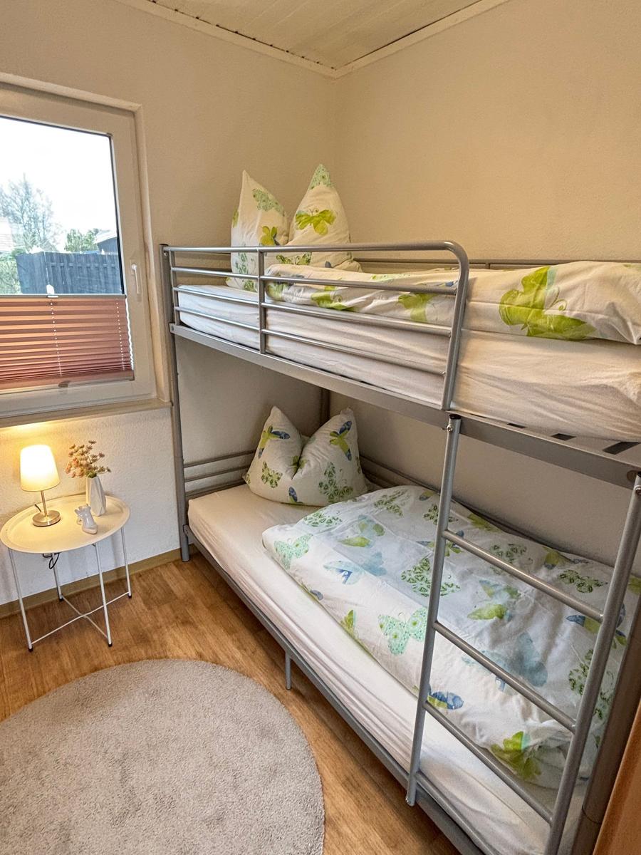 Zimmer mit Doppelstockbett, Fenster und kleinem Tisch mit Lampe.