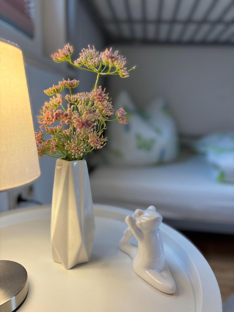 Auf dem Nachttisch steht eine weiße Vase mit Blumen und eine Katzenfigur.