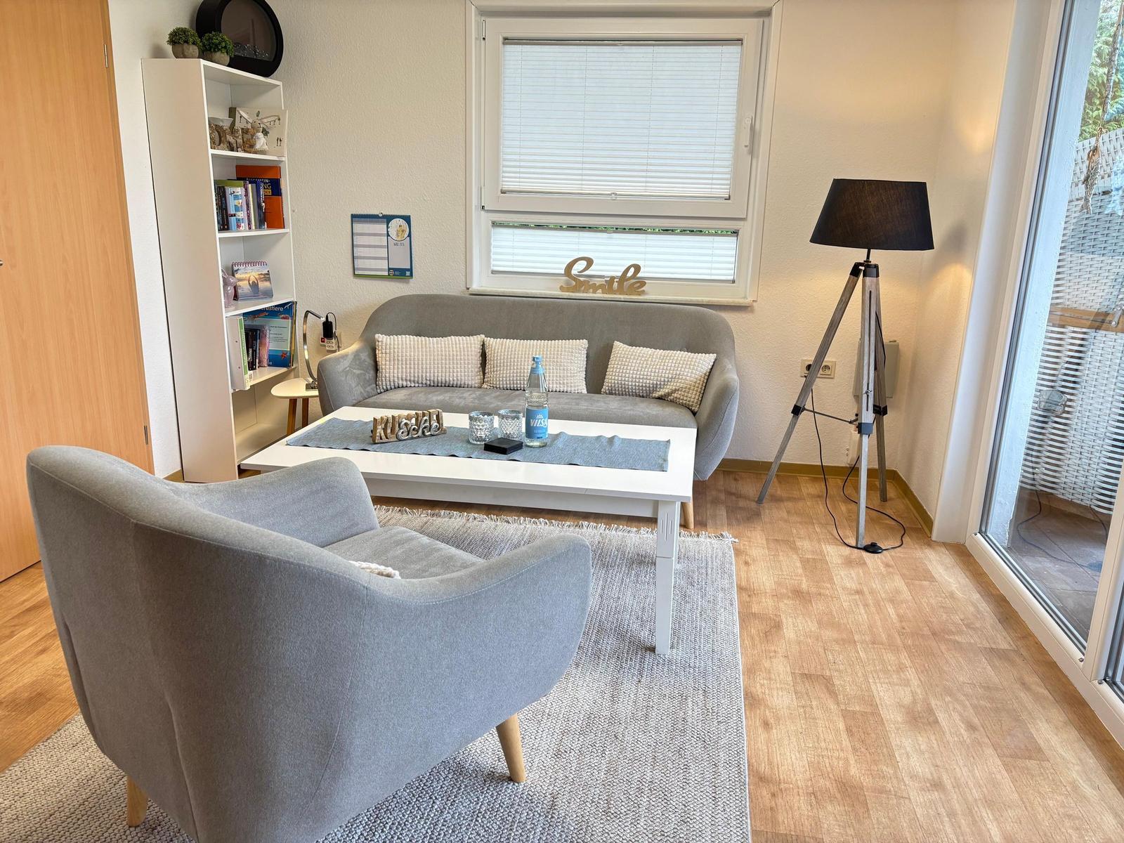 Wohnzimmer mit Sofa, Sessel, Tisch und Fenster.
