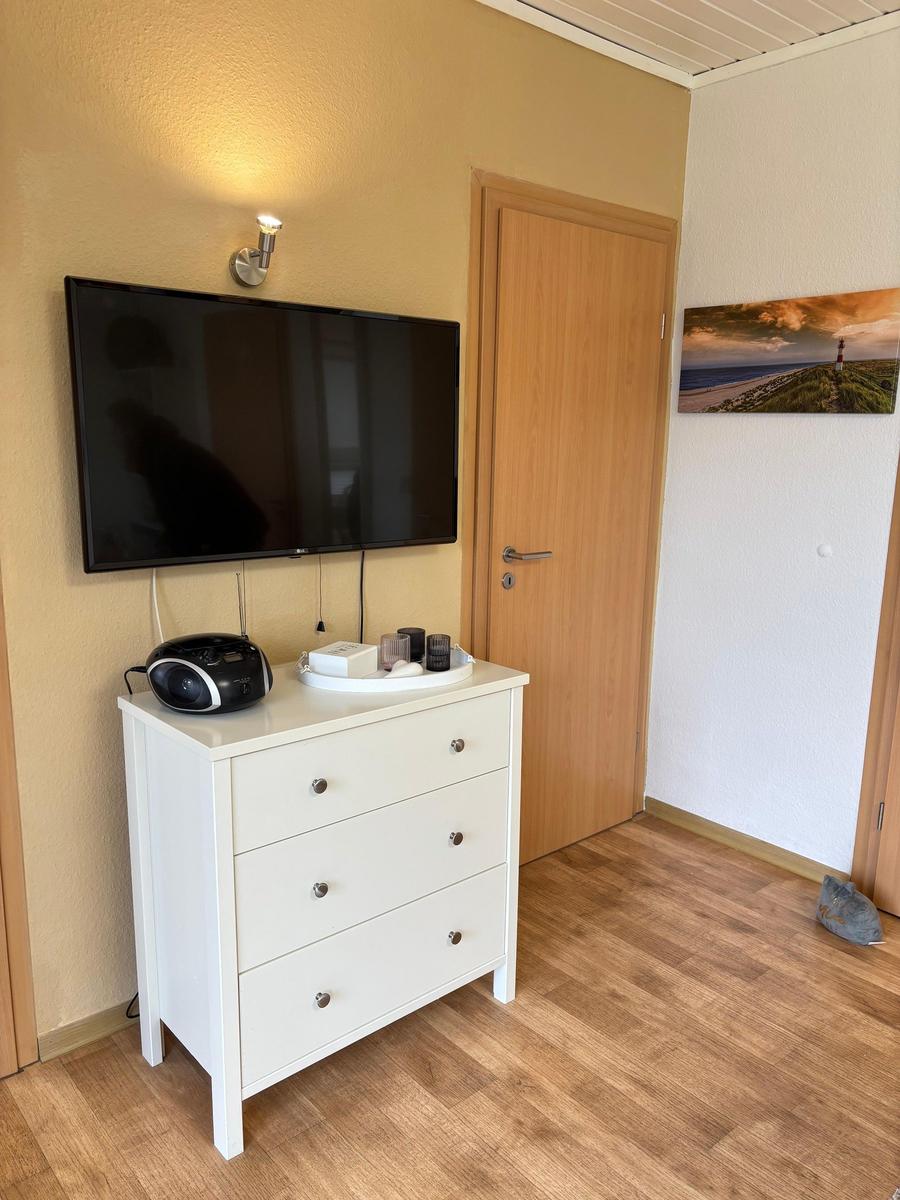 Schlafzimmer mit TV, Schrank und Tür. Wandbild zeigt Leuchtturm.