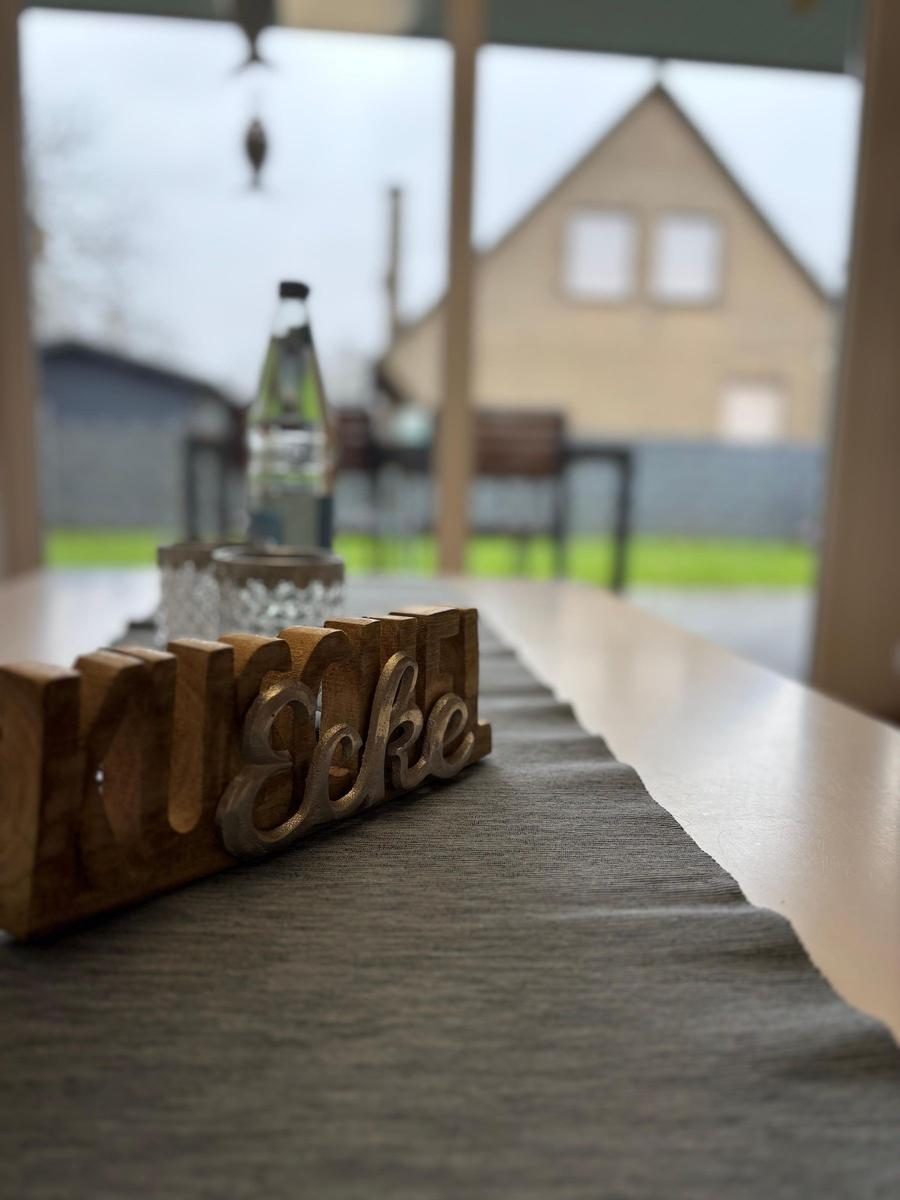Holztablett mit Schriftzug auf Tisch, Blick auf Gartenhaus im Hintergrund.