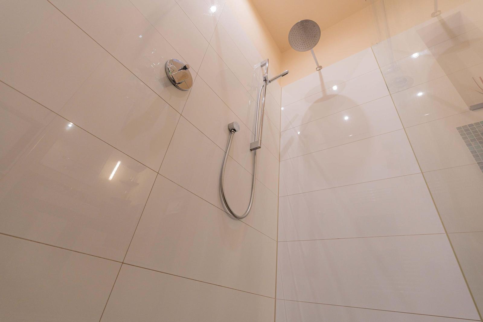 Dusche mit Duschbrause und Handbrause an glatten Fliesenwänden.