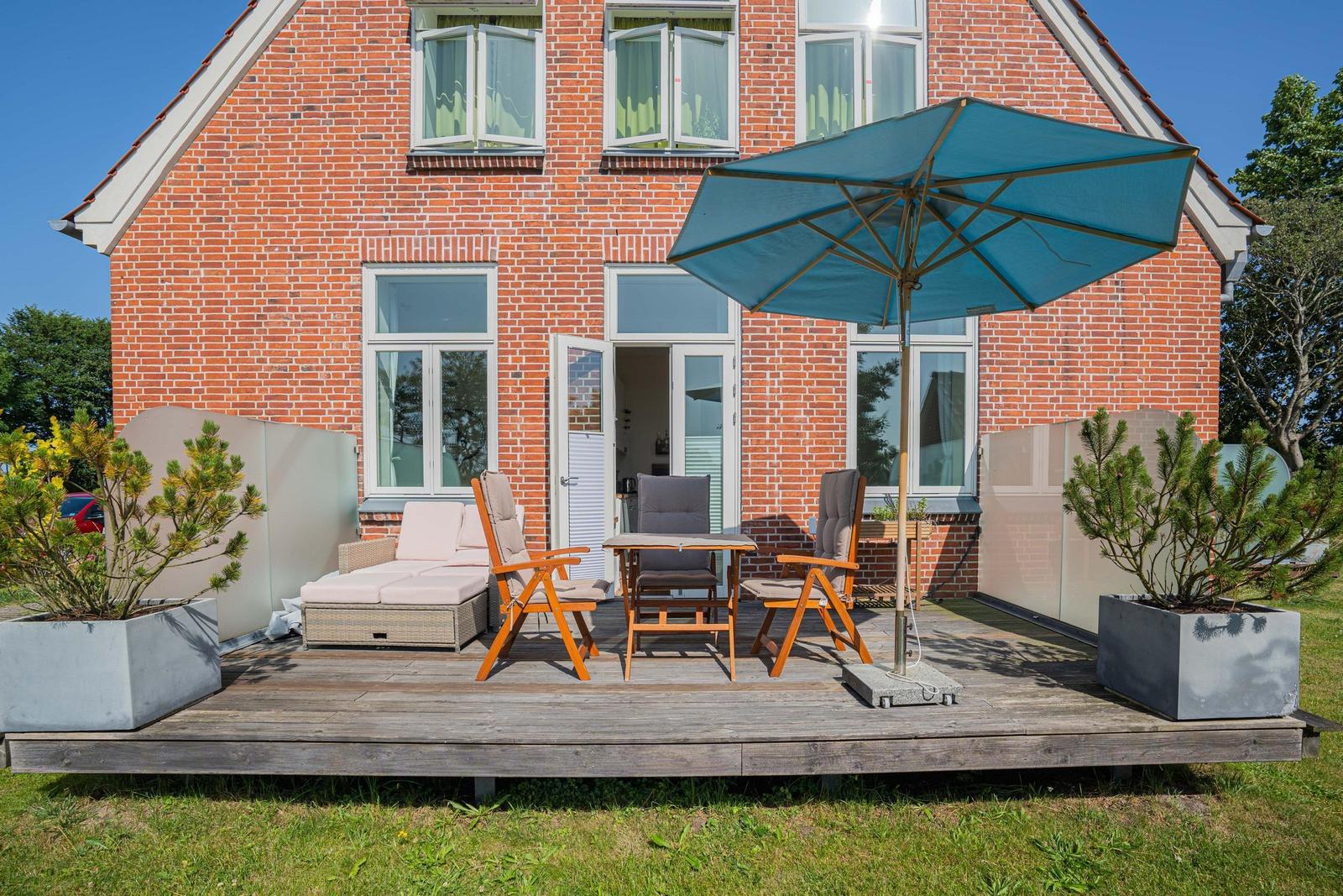 Holzterrasse mit Sitzgruppe, Sonnenschutz und Pflanzen vor einem Backsteinhaus.