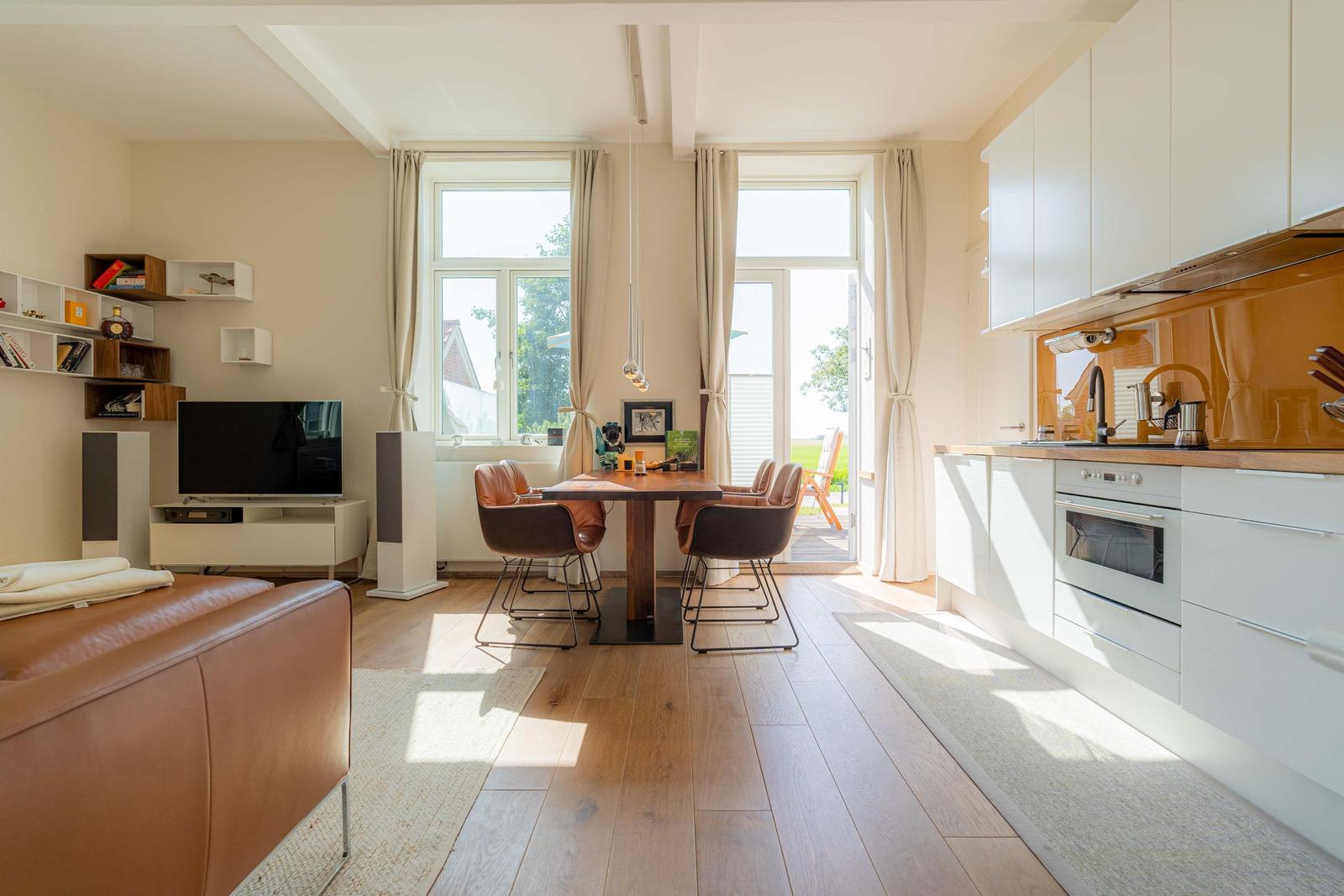 Wohn- und Essbereich mit Küche, Holzboden und Fenstern zum Garten.