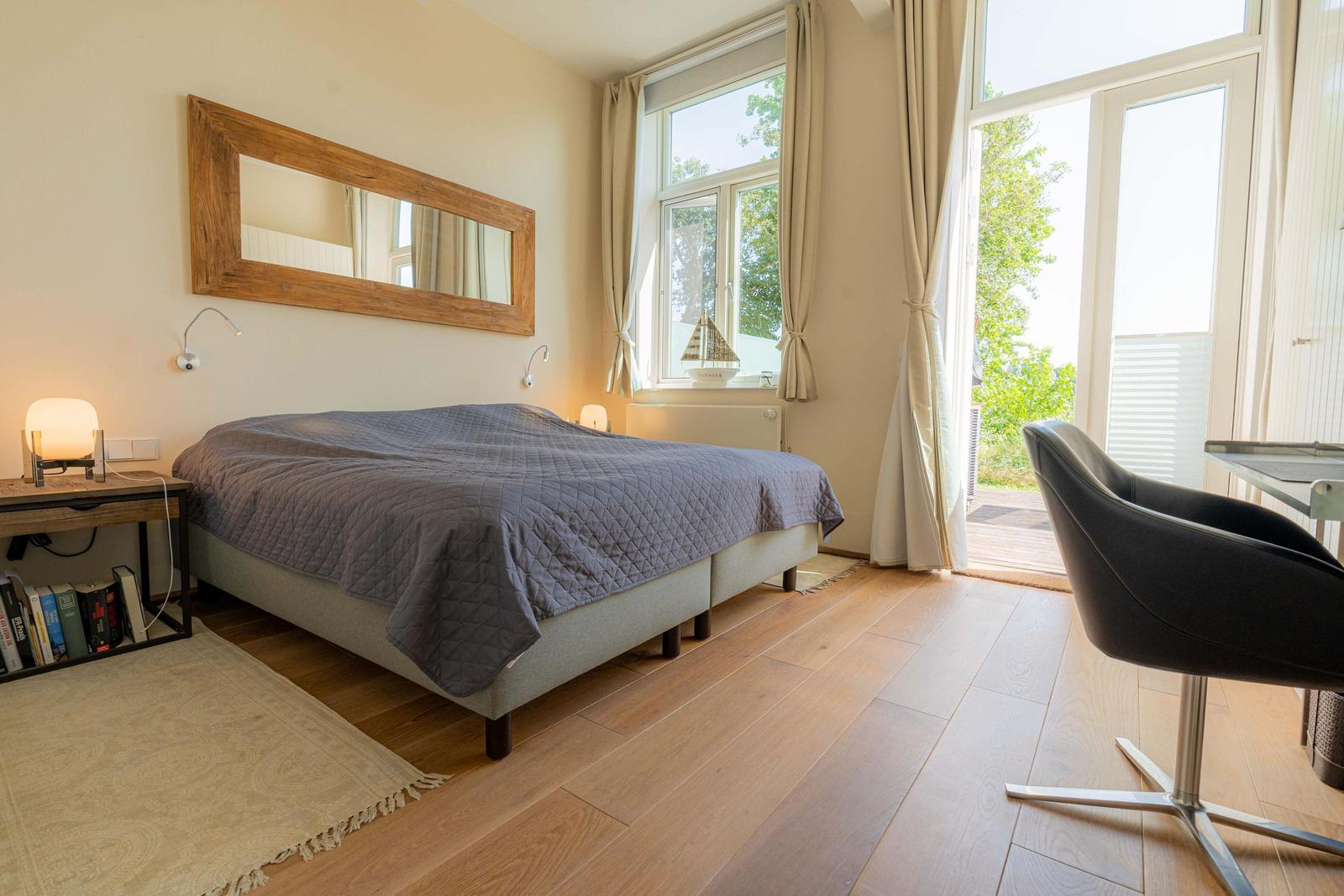 Schlafzimmer mit Bett, Spiegel, Schreibtisch und Balkontür.
