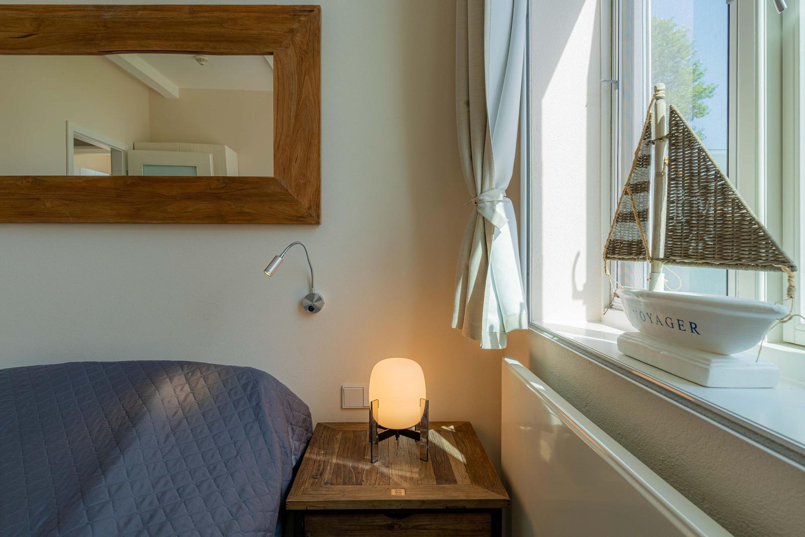 Bett mit Nachttisch, Spiegel und Segelschiffmodell am Fenster