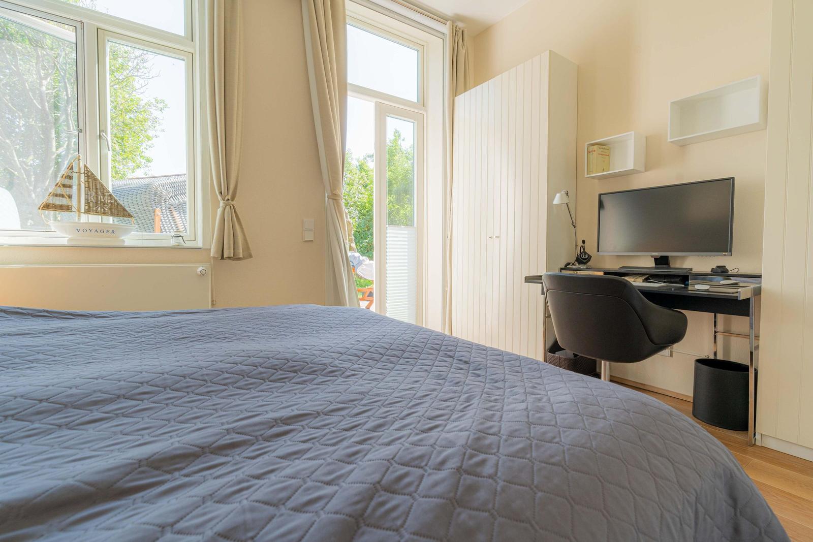 Schlafzimmer mit Bett, Schreibtisch und Fenster zum Garten.