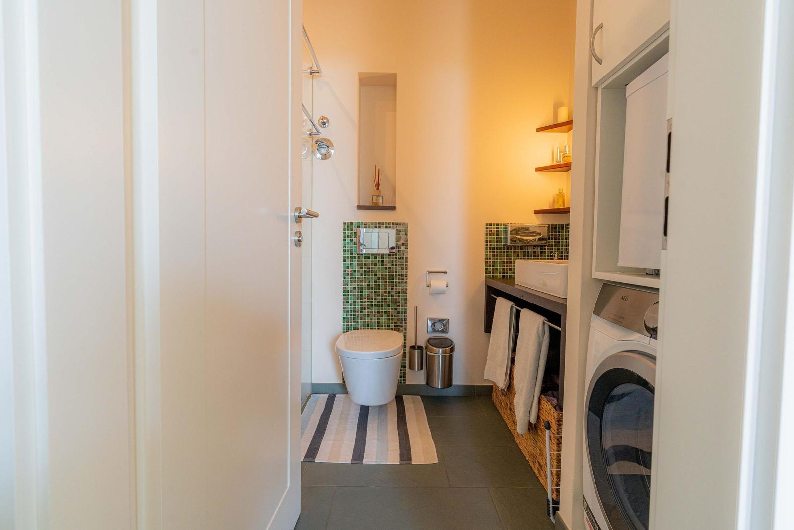 Badezimmer mit Toilette, Dusche, Waschmaschine und Handtuchkorb.