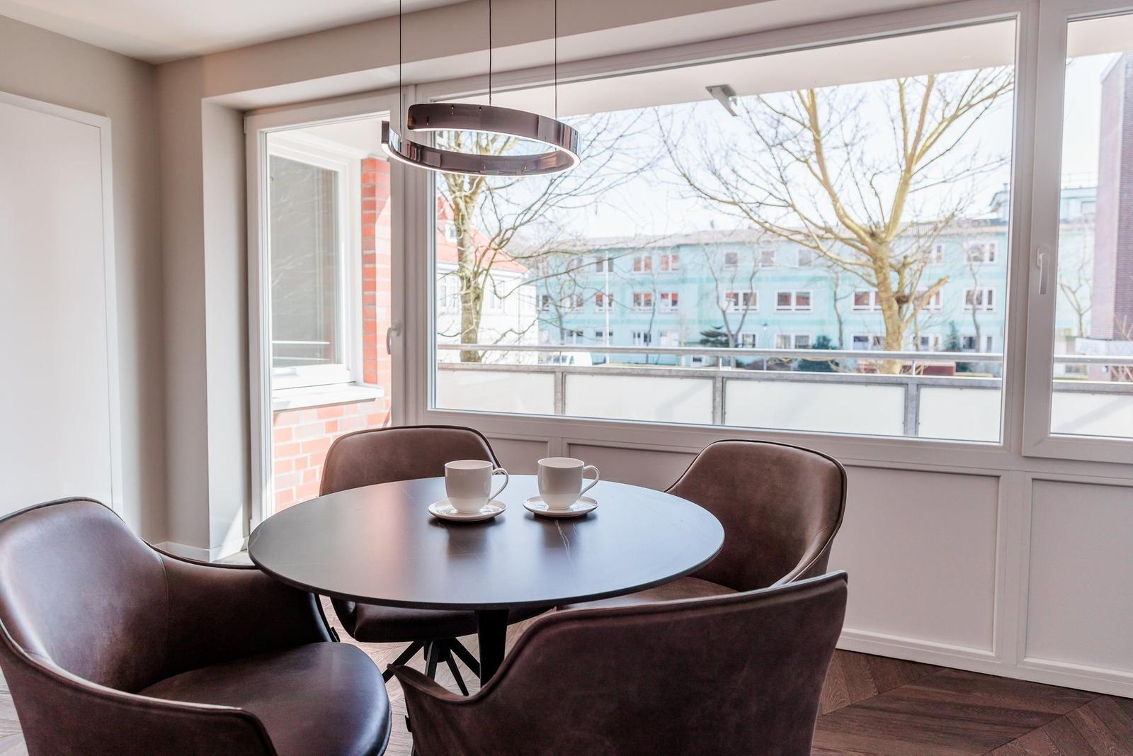 Runder Tisch mit vier Stühlen vor großem Fenster mit Blick auf Gebäude.