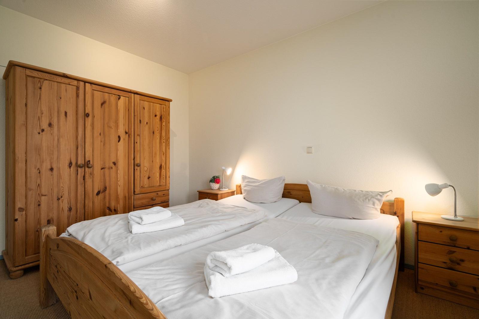 Zimmer mit Doppelbett, Holzkommode und Nachttischen mit Lampen.