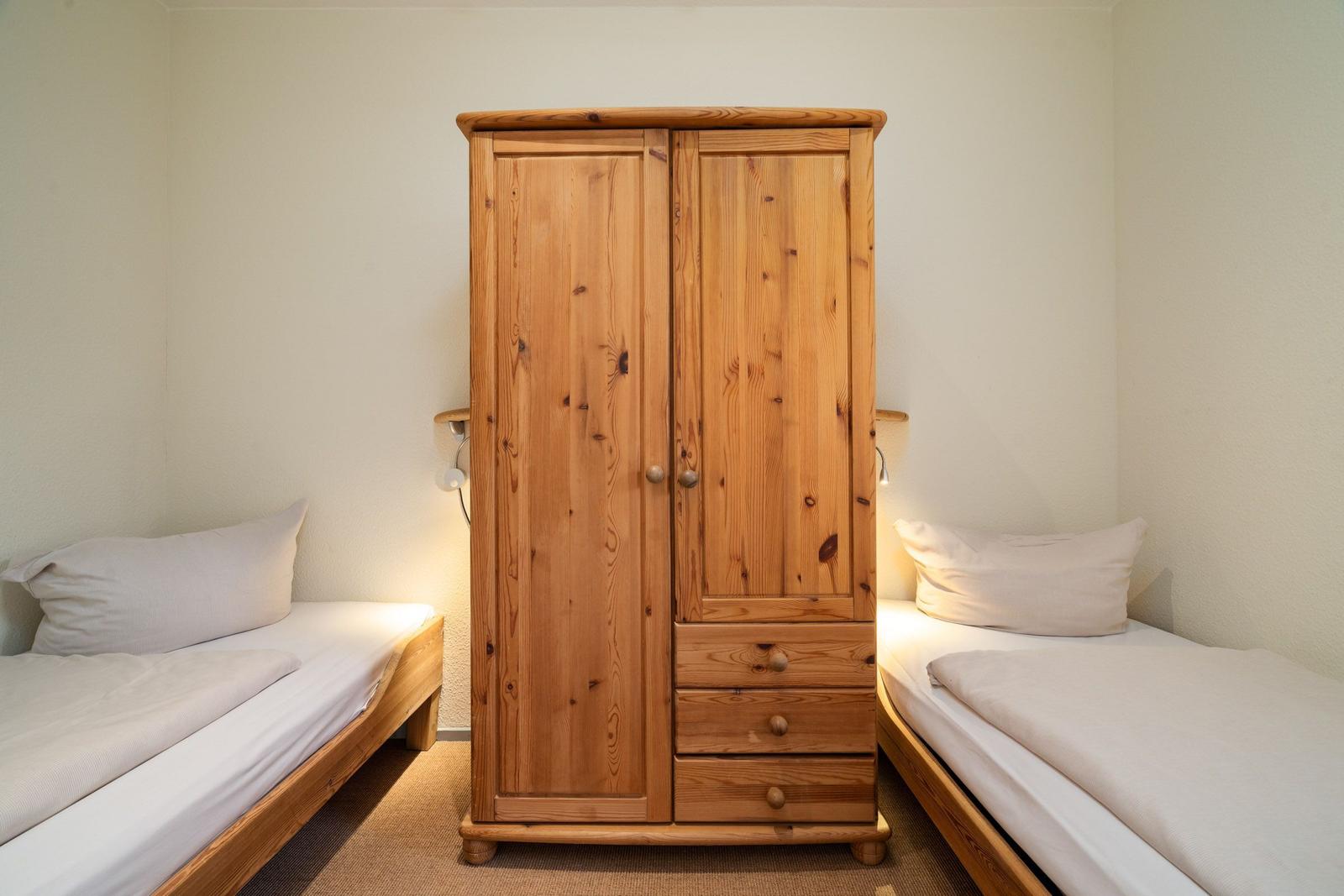 Zwei Einzelbetten flankieren einen Holzschrank mit Schubladen.