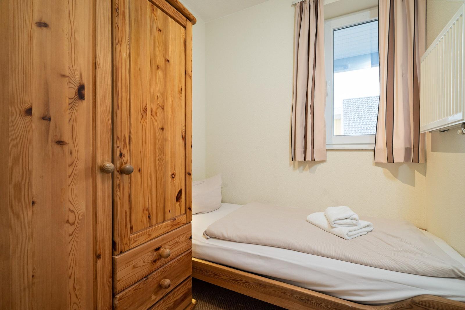 Schlafzimmer mit Holzschrank, Bett und Fenster mit Vorhängen.