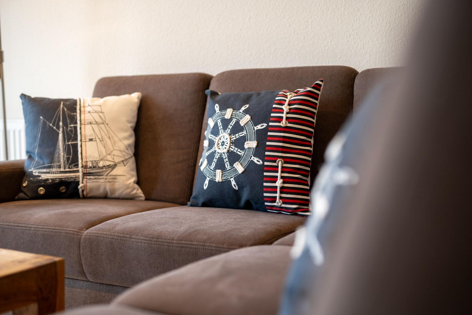 Ein braunes Sofa mit zwei Kissen, eines mit Segelschiff, das andere mit Ruder