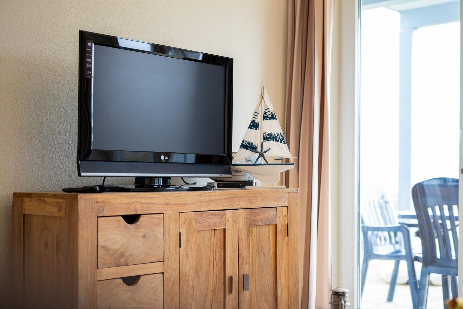 TV auf Holzschrank mit Segelschiffmodell und Blick auf Terrasse