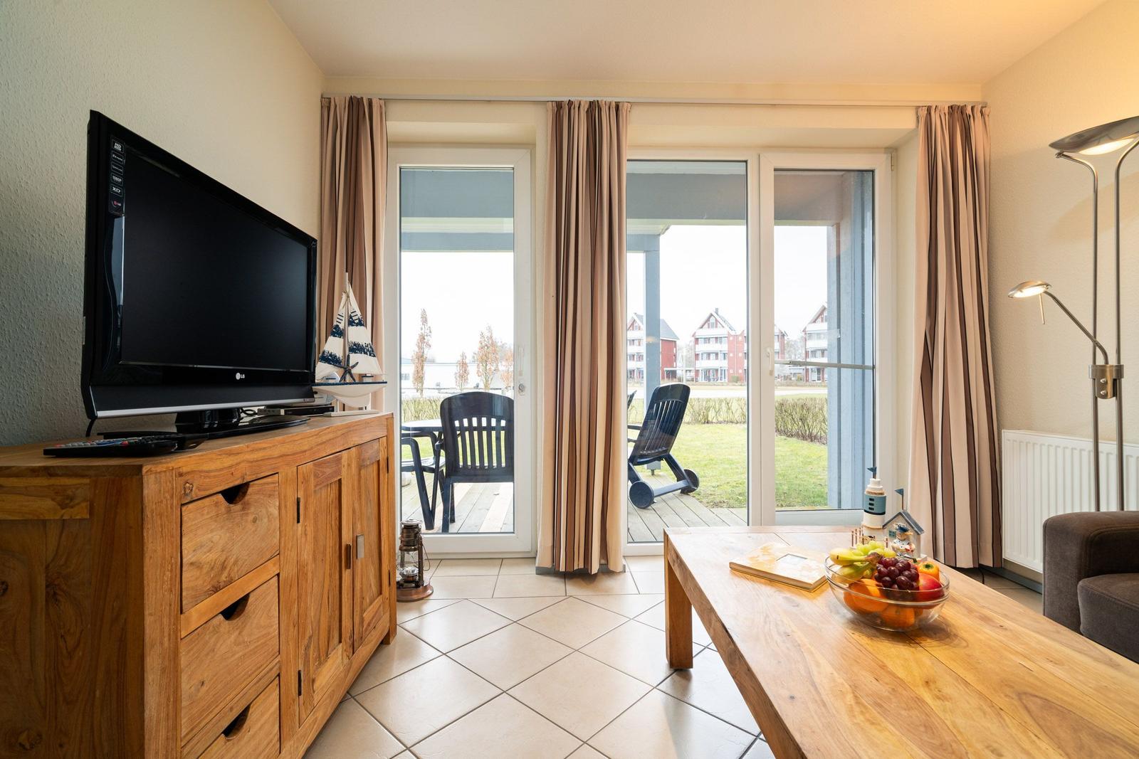 Wohnzimmer mit Fernseher, Holztisch und Blick auf die Terrasse.