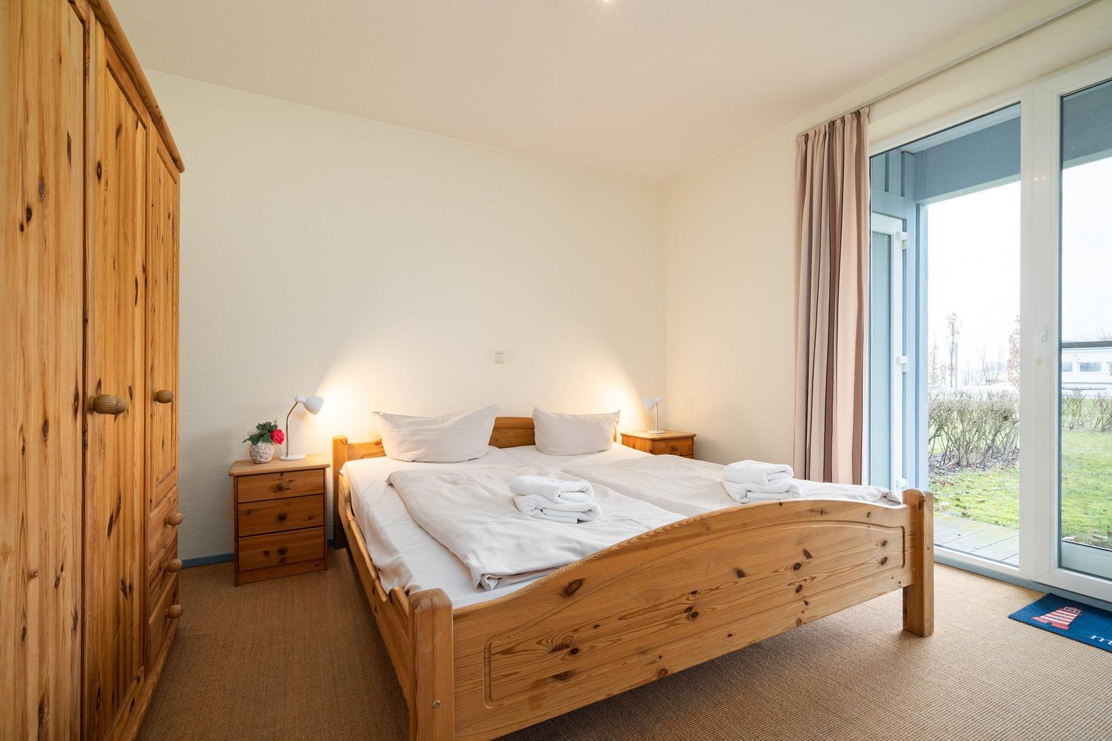 Schlafzimmer mit Holzbett, Schrank und Balkontür.