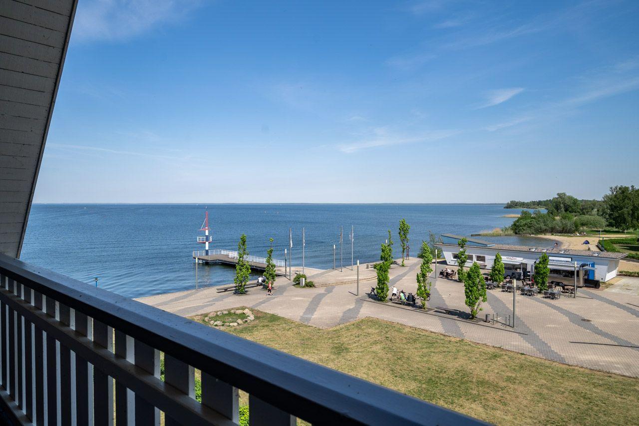Blick vom Balkon auf See, Pier und Strandbereich mit Sitzgelegenheiten.
