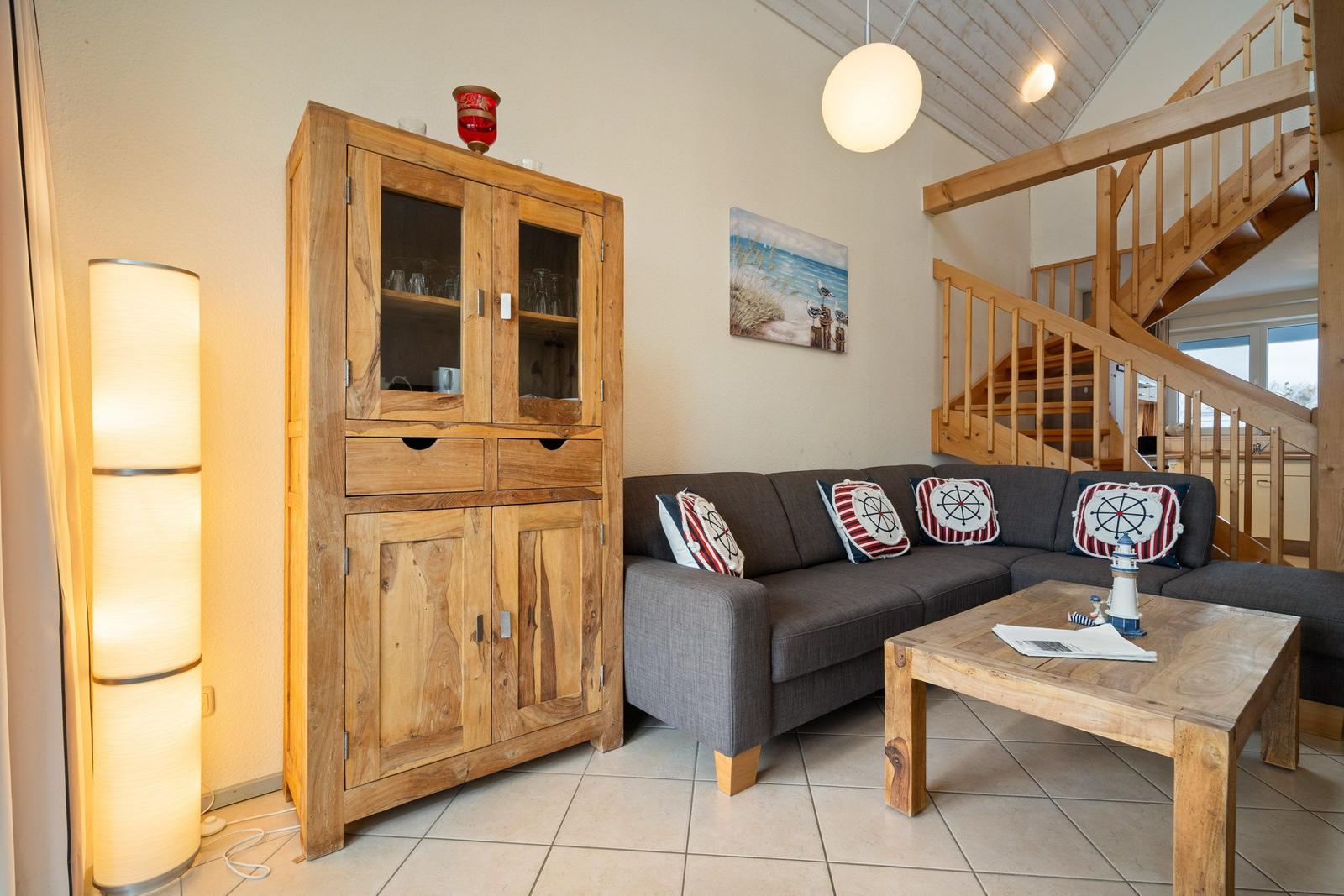 Wohnzimmer mit Sofa, Holzregal und Treppe zur oberen Etage.