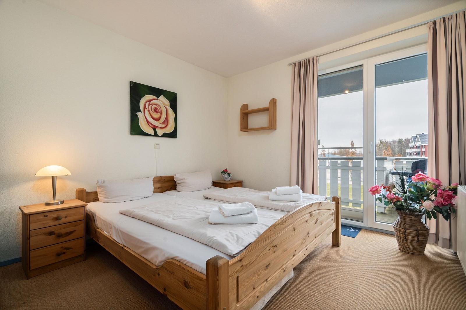 Schlafzimmer mit Holzbett, Nachttisch und Balkonansicht.