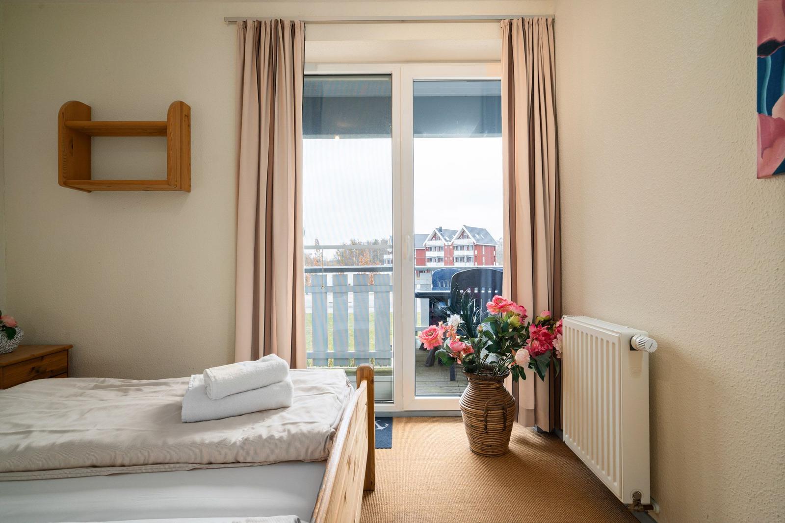 Schlafzimmer mit Balkon, Bett, Blumen und Heizkörper.