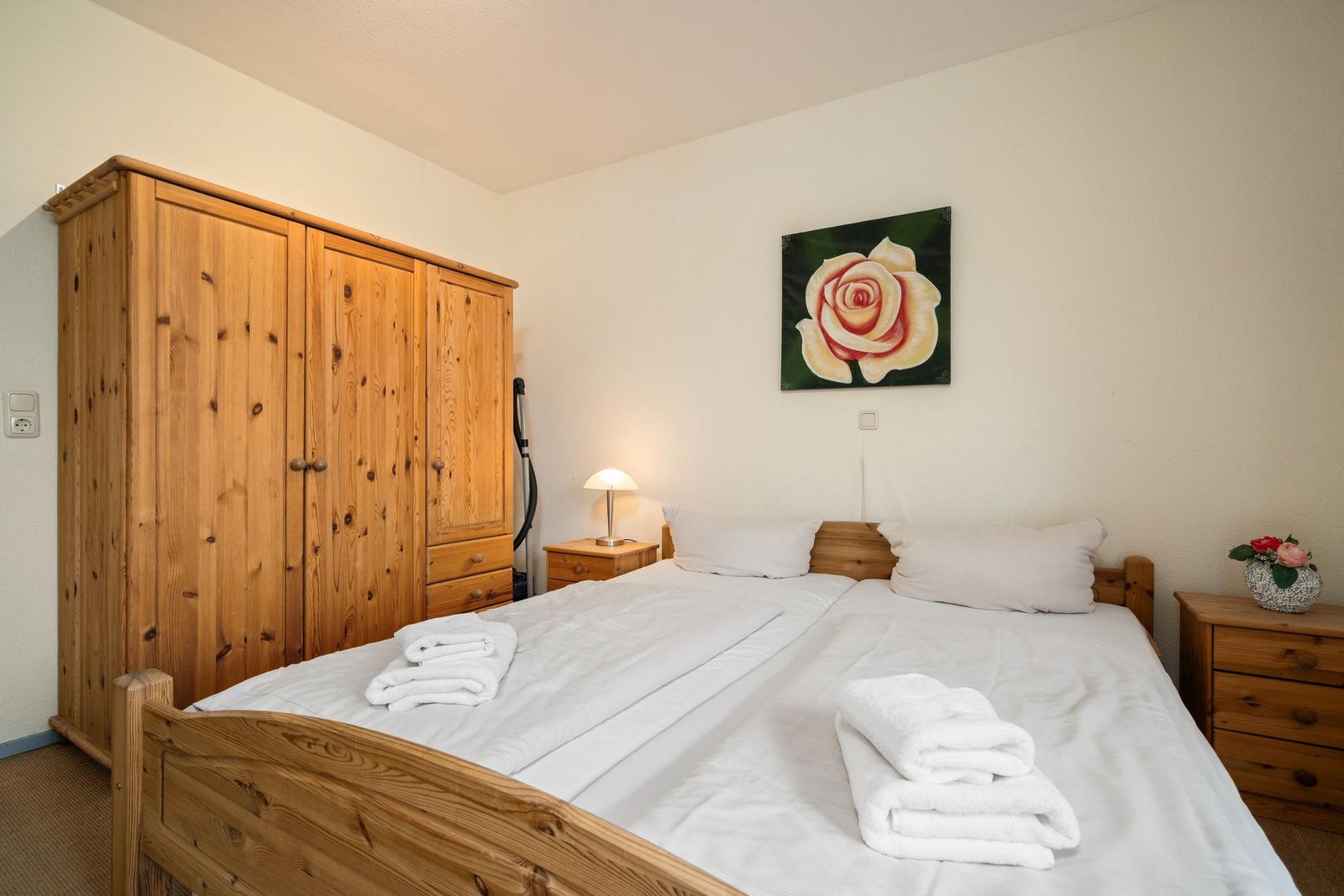 Schlafzimmer mit Holzbett, Kleiderschrank und Nachttisch. Auf dem Bett liegen gefaltete Handtücher.