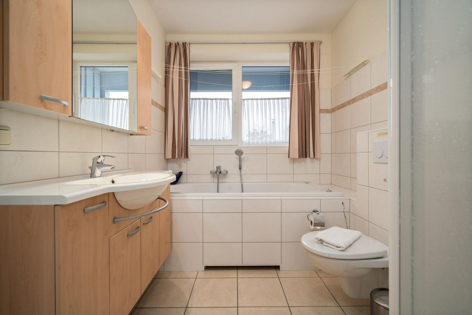 Bad mit Badewanne, Waschbecken und Toilette. Fenster mit Vorhängen.