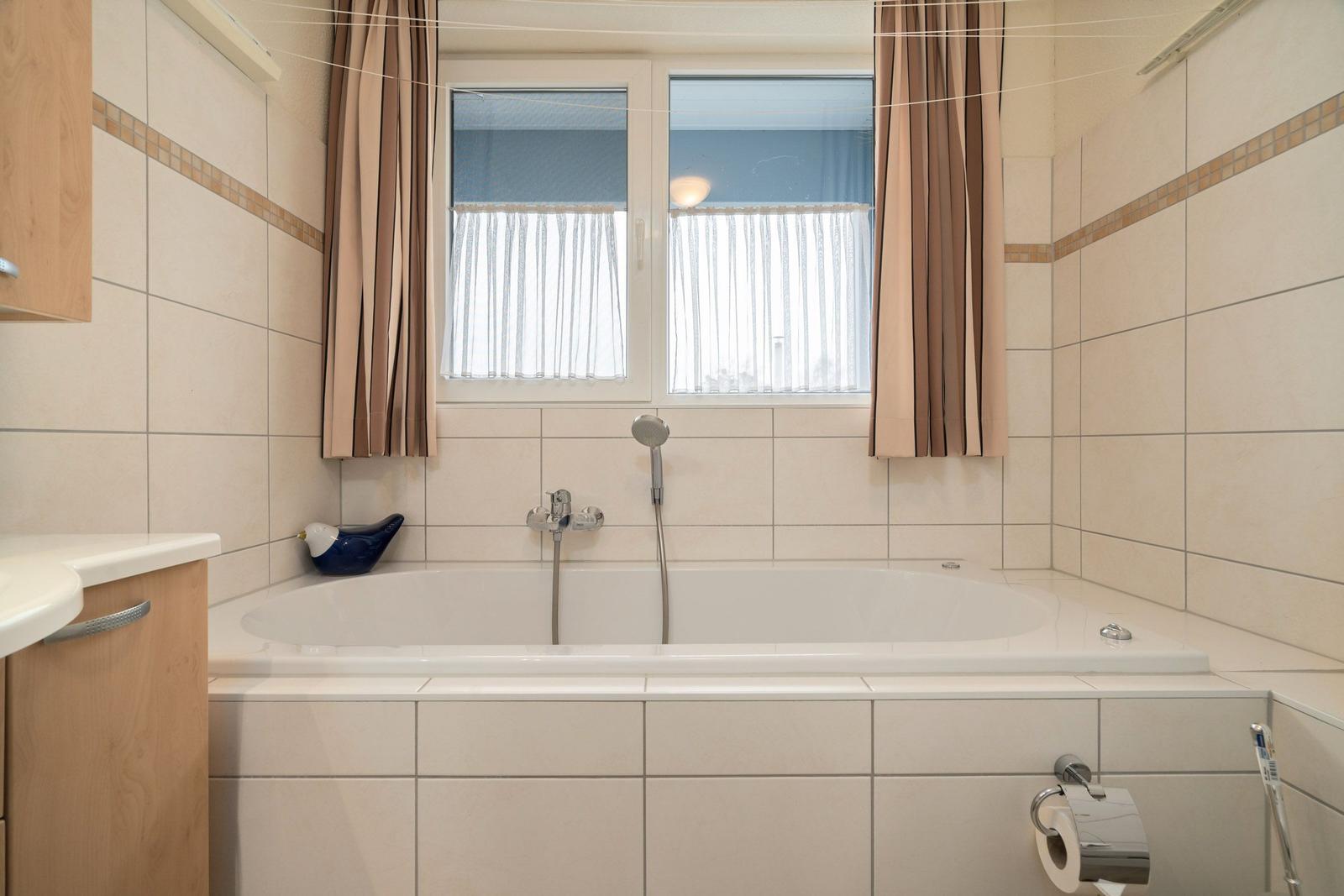 Bad mit Badewanne, Fenster und Holzschränken.