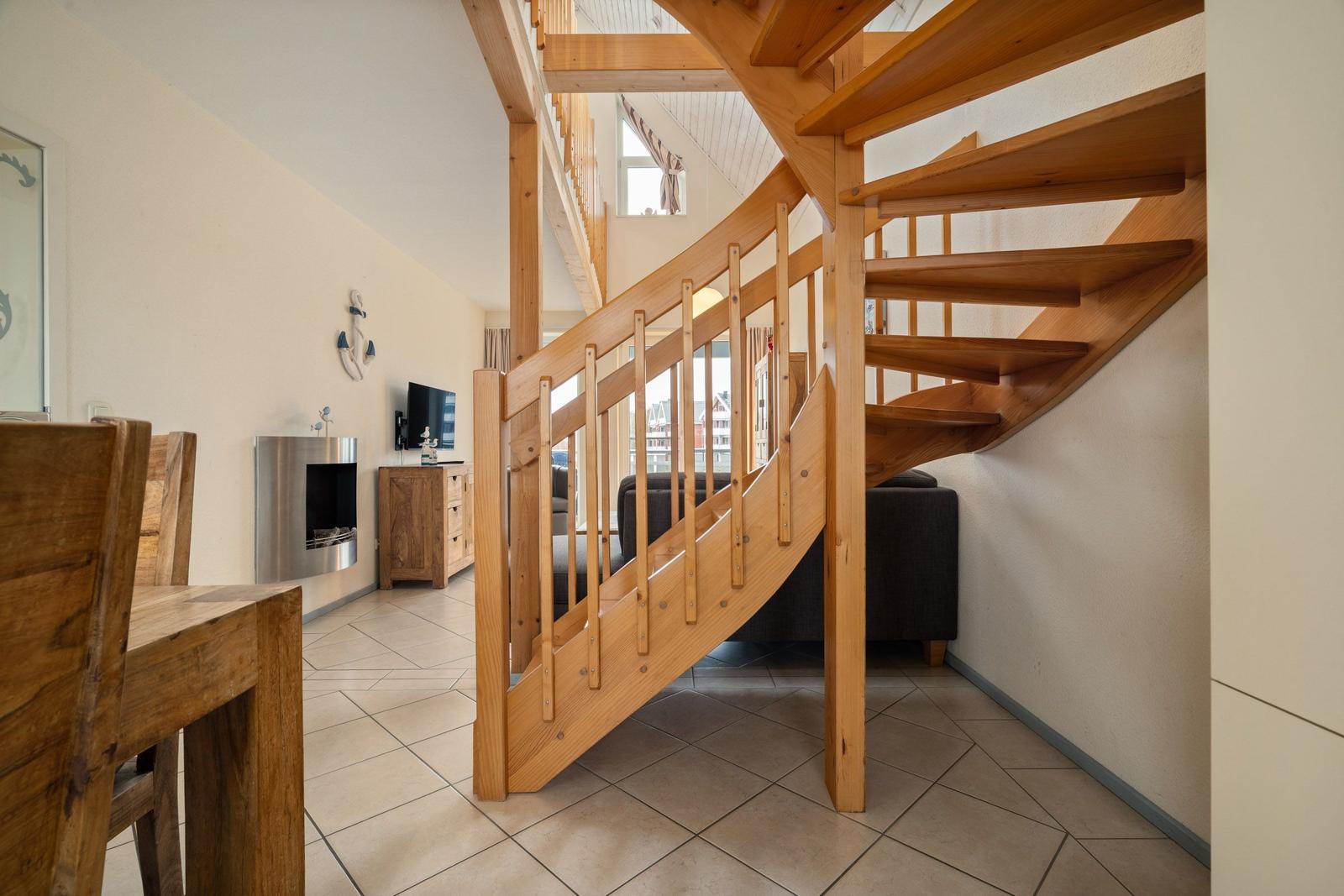 Holzspindeltreppe führt zur oberen Etage. Im Hintergrund Wohnzimmer mit Sofa und Fernseher.