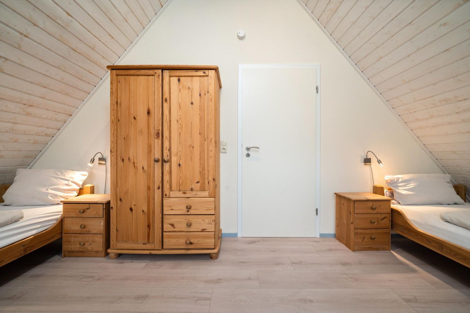 Zimmer mit zwei Betten, Holzschrank und Schreibtisch unter schrägen Dachschrägen.