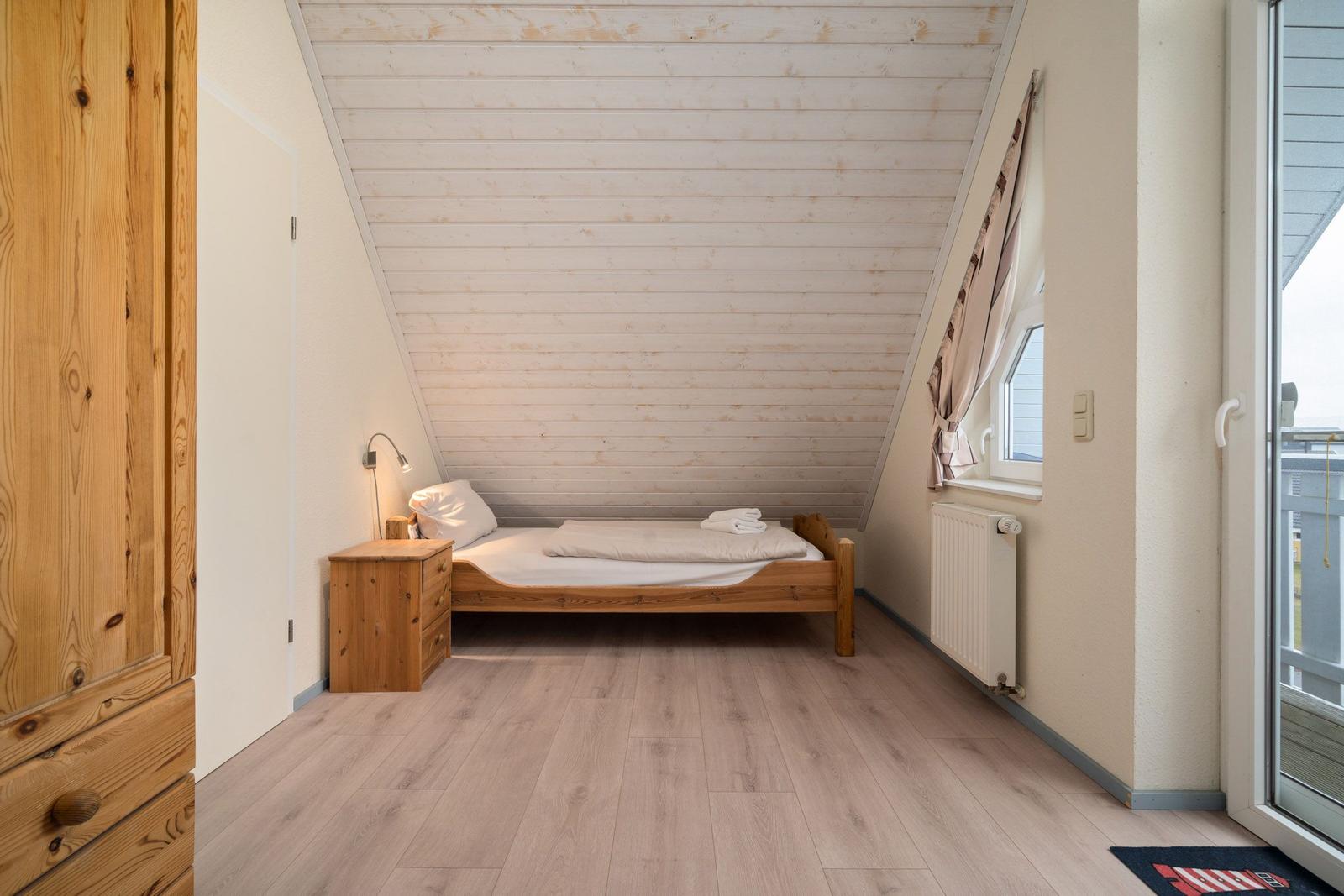 Schlafzimmer mit Holzbett, Schrank und Fenster. Dachschräge und Holzfußboden.