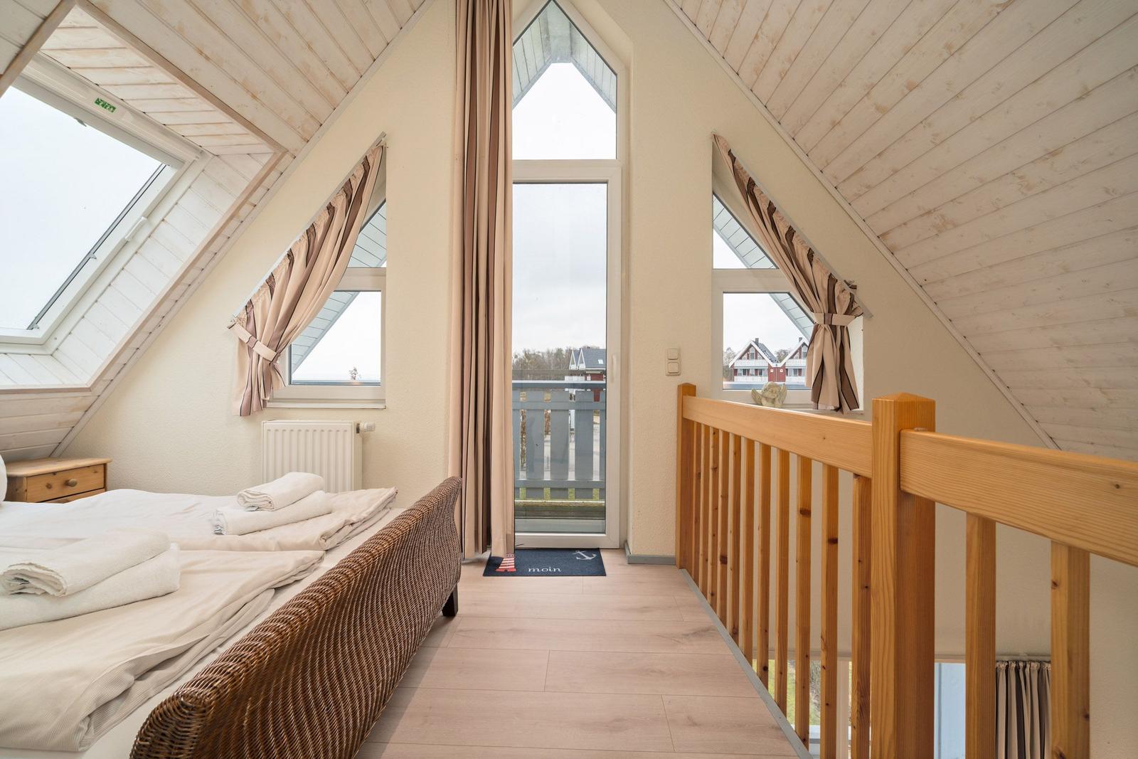 Dachgeschosszimmer mit Bett, Fenstern und Balkonzugang.