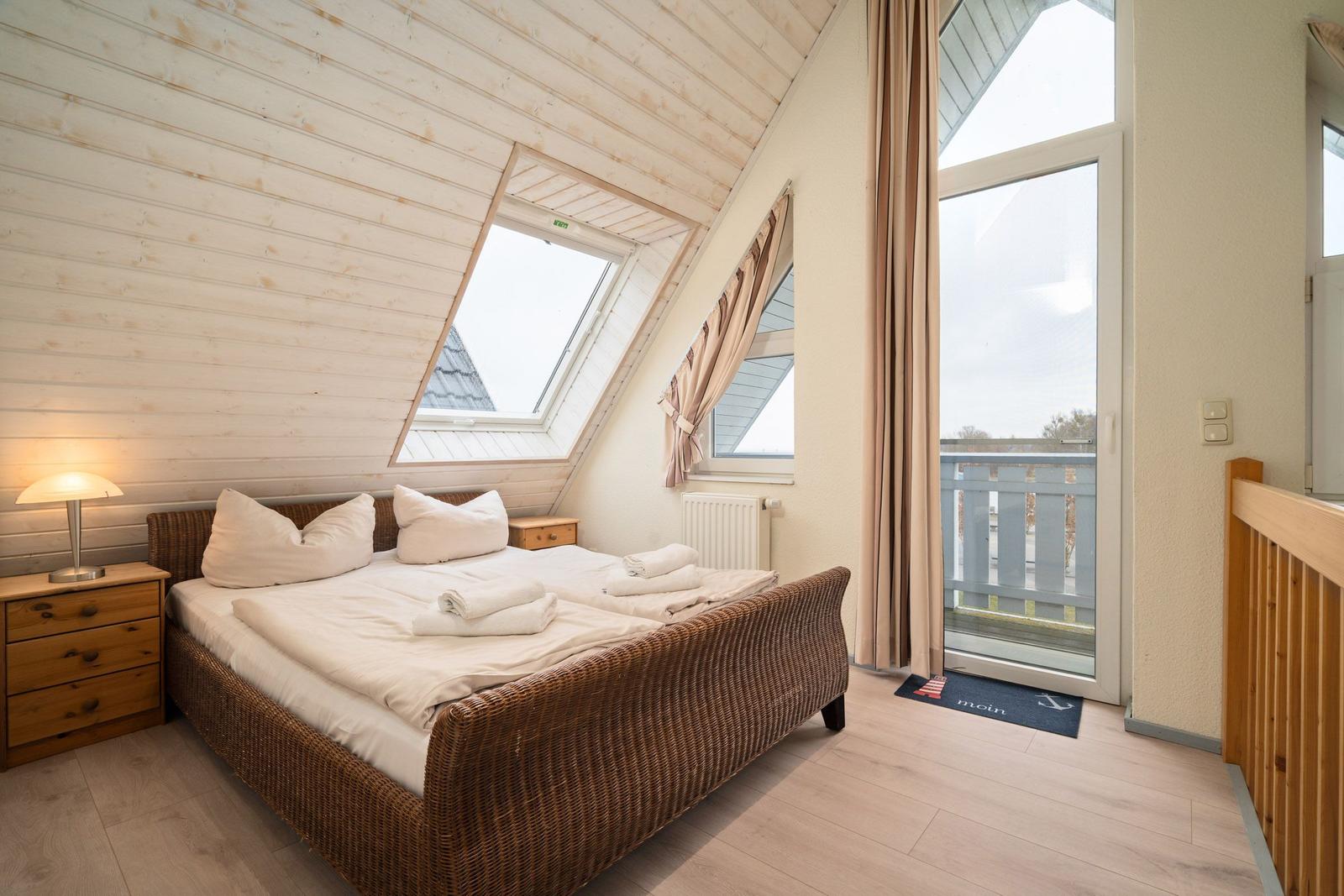 Schlafzimmer mit Dachschrägen, Bett, Fenster und Balkonzugang.