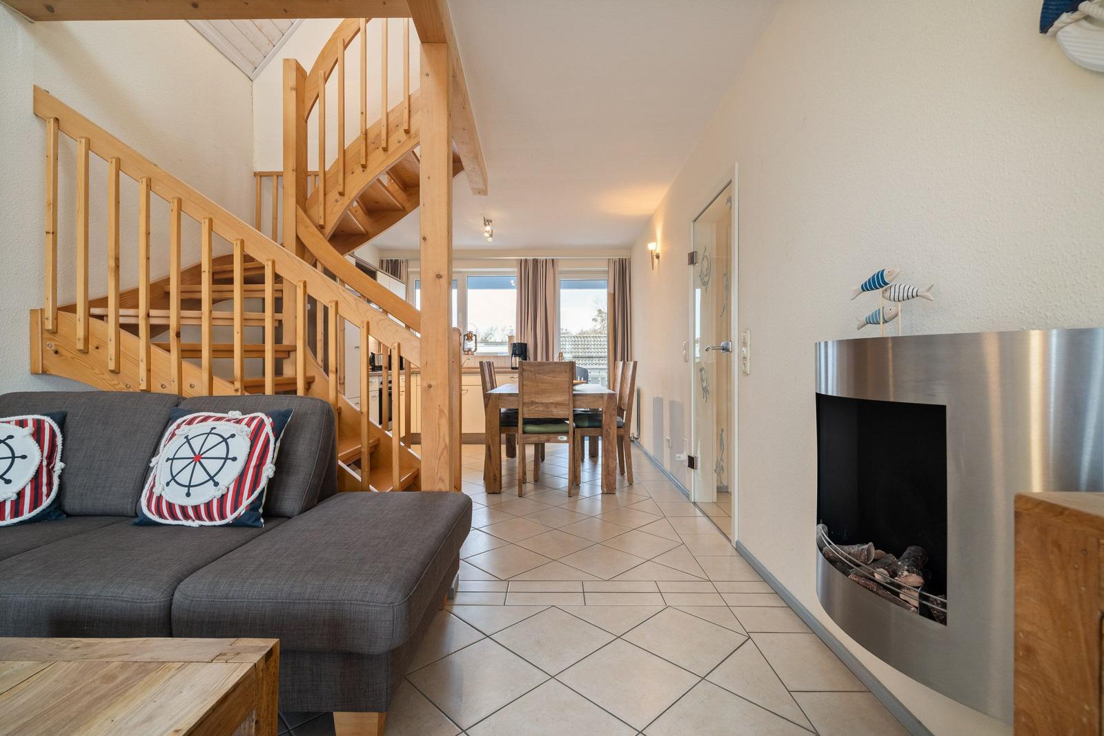 Wohnzimmer mit Sofa, Kamin und Holztreppe zur oberen Etage.