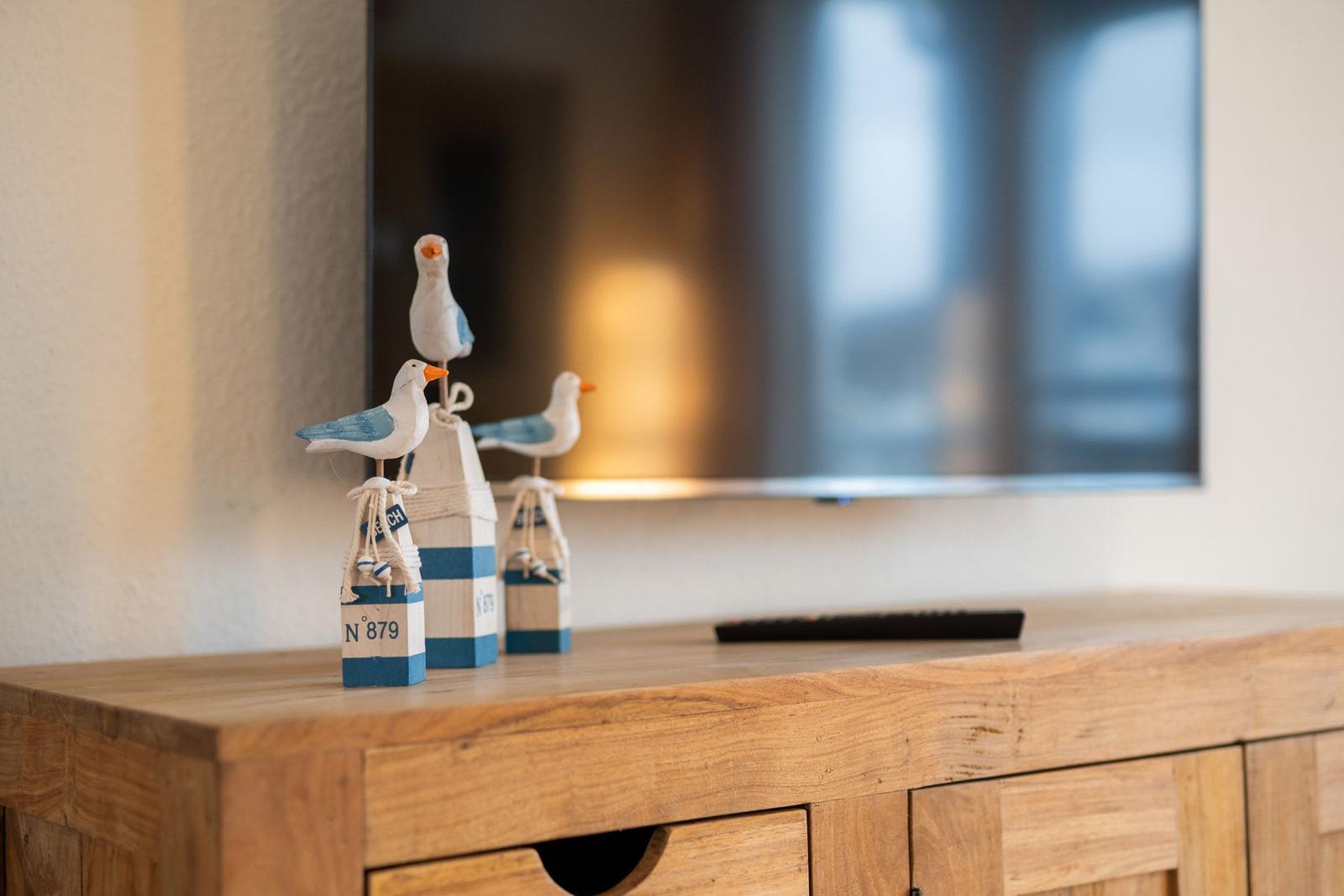 Holzkommode mit Vogeldekoration und Fernseher im Hintergrund.