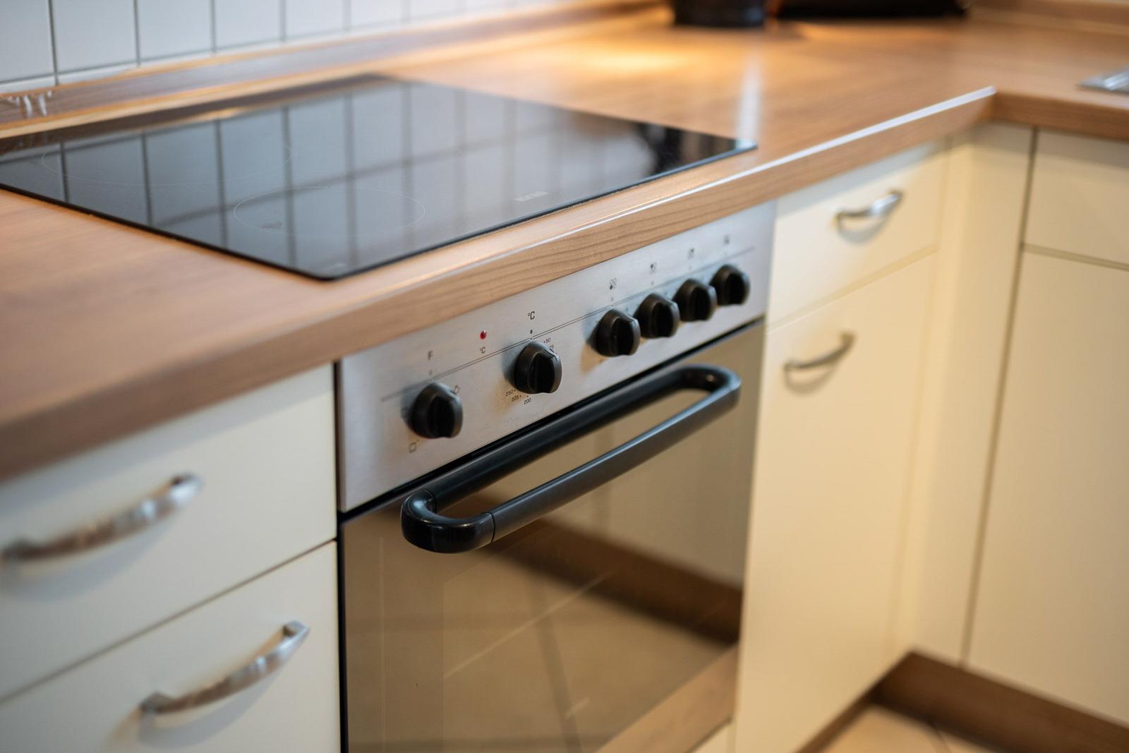 Küche mit Induktionskochfeld und Backofen. Holzoberfläche und weiße Schränke.