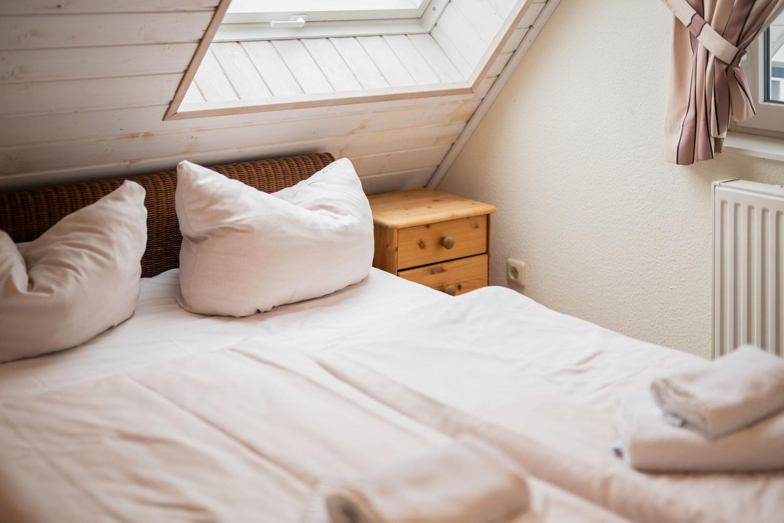 Schlafzimmer mit Dachschrägen, Bett, Nachttisch und Dachfenster.