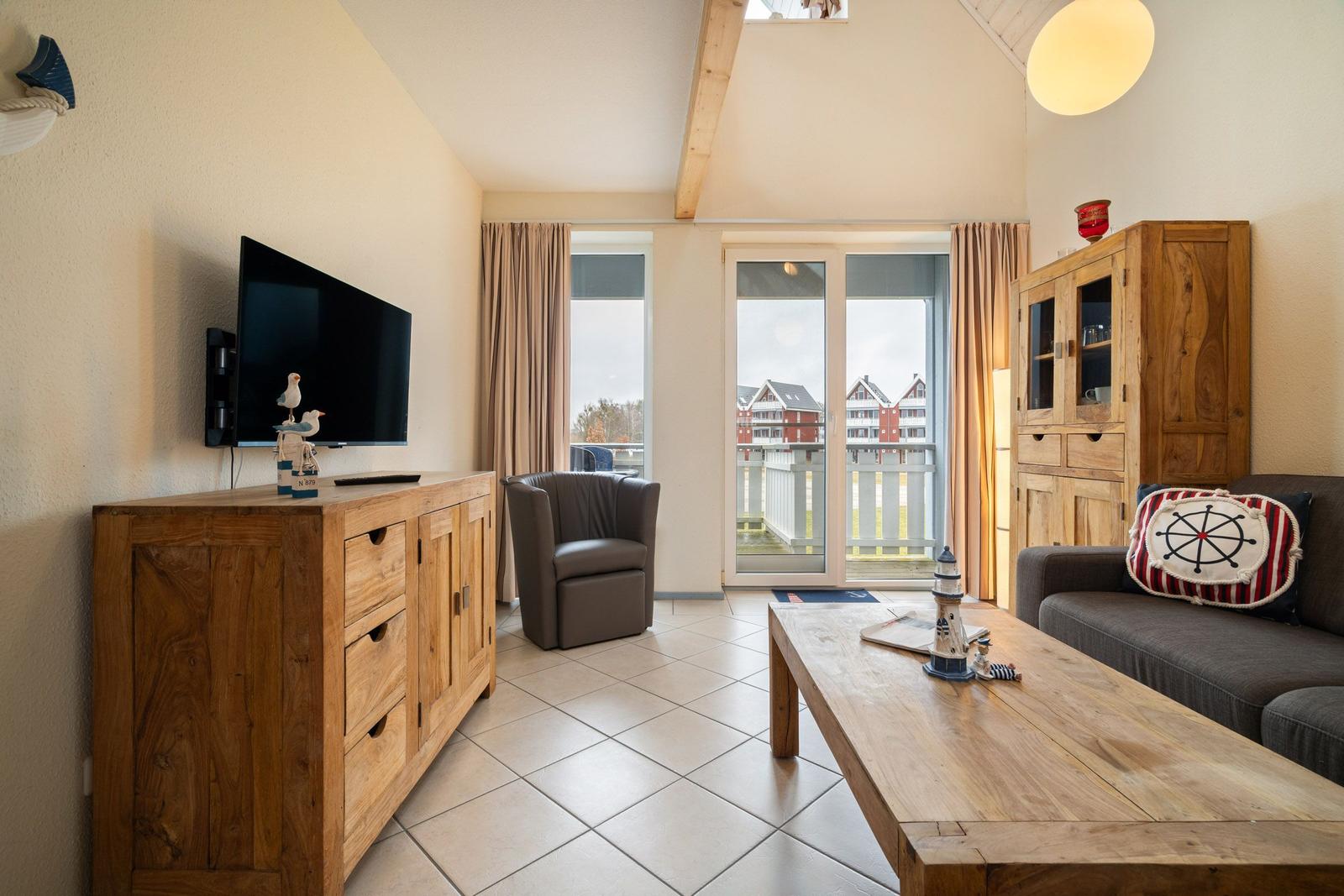 Wohnzimmer mit Holzmöbeln, Fernseher und Balkonansicht.