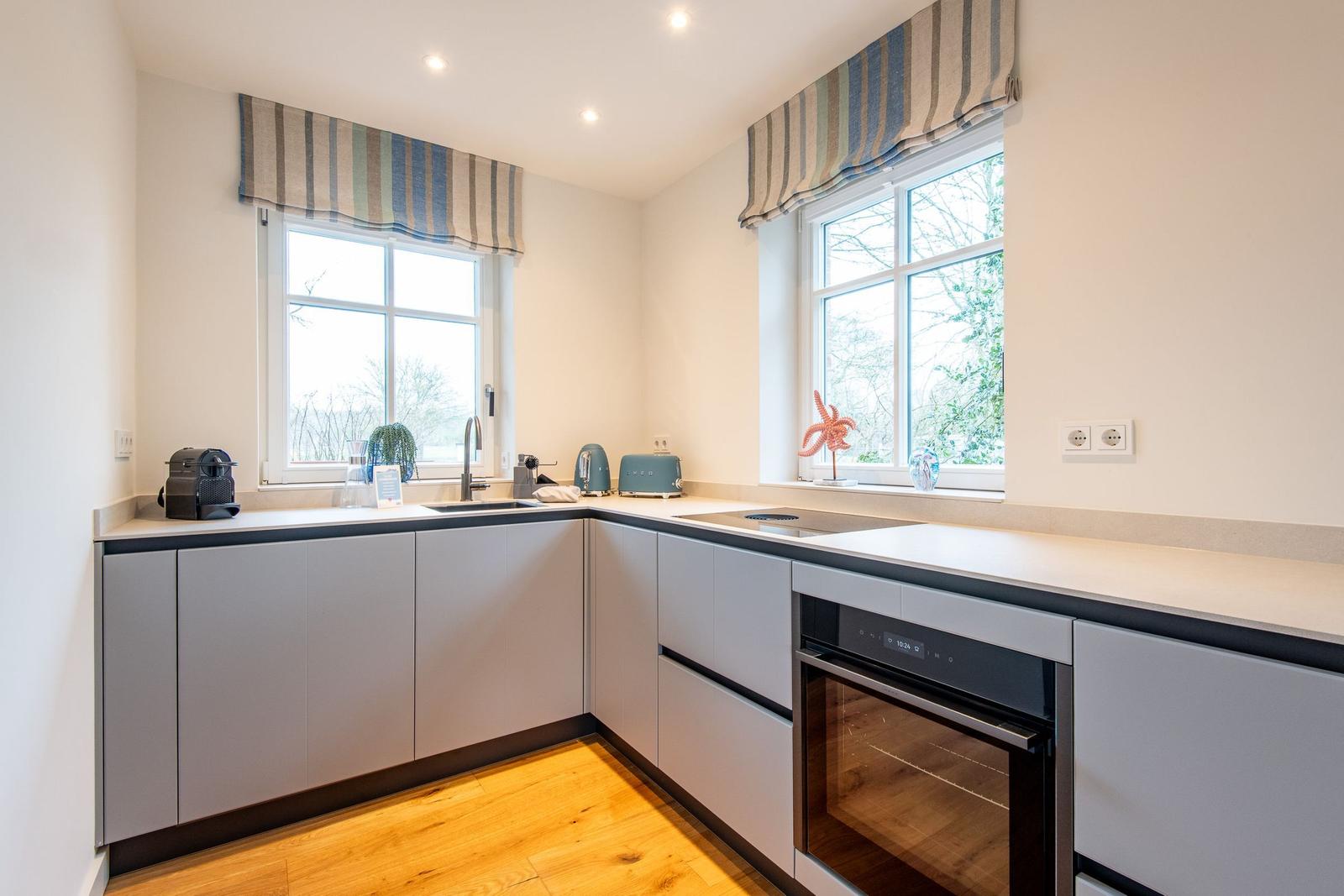 Moderne Küche mit zwei Fenstern, grauen Schränken und integriertem Backofen.