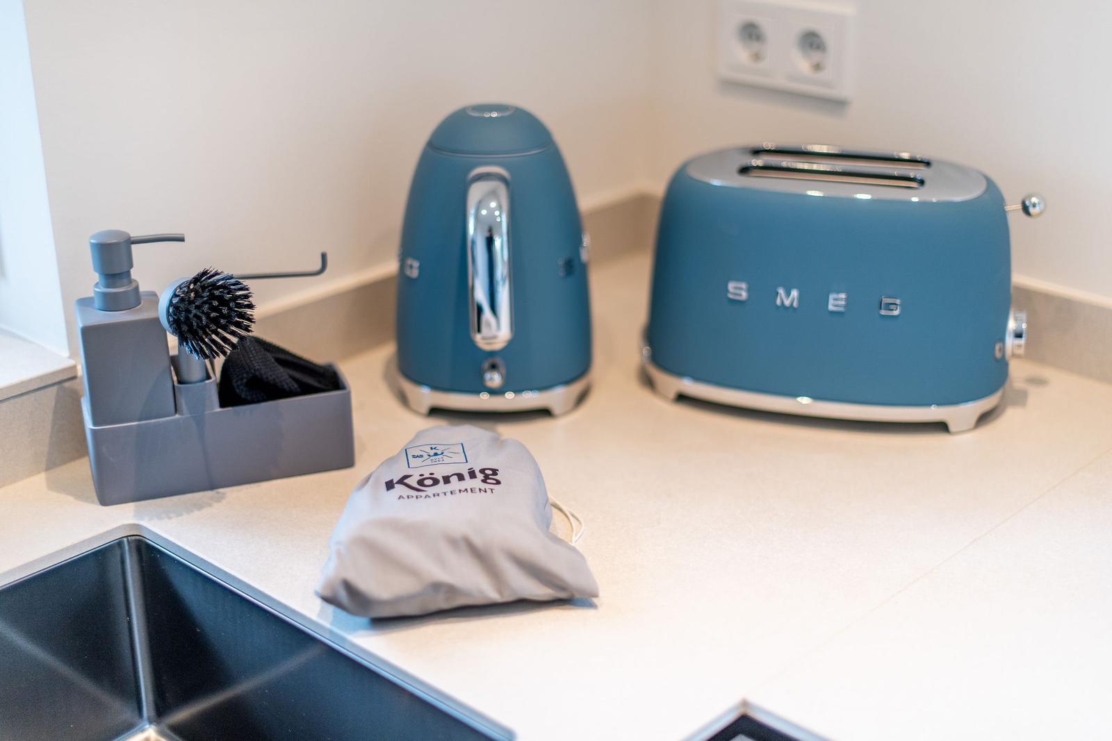 Küchenzeile mit Kaffeemaschine und Toaster. Reinigungsmittel und Tasche für Gäste.